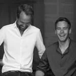 Snow-capped mountains with a small building on a grassy hill in the foreground.