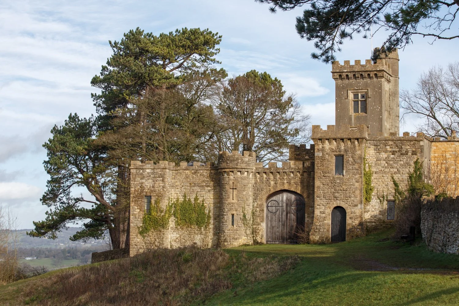 Stone castle with tower and arched wooden door surrounded by trees