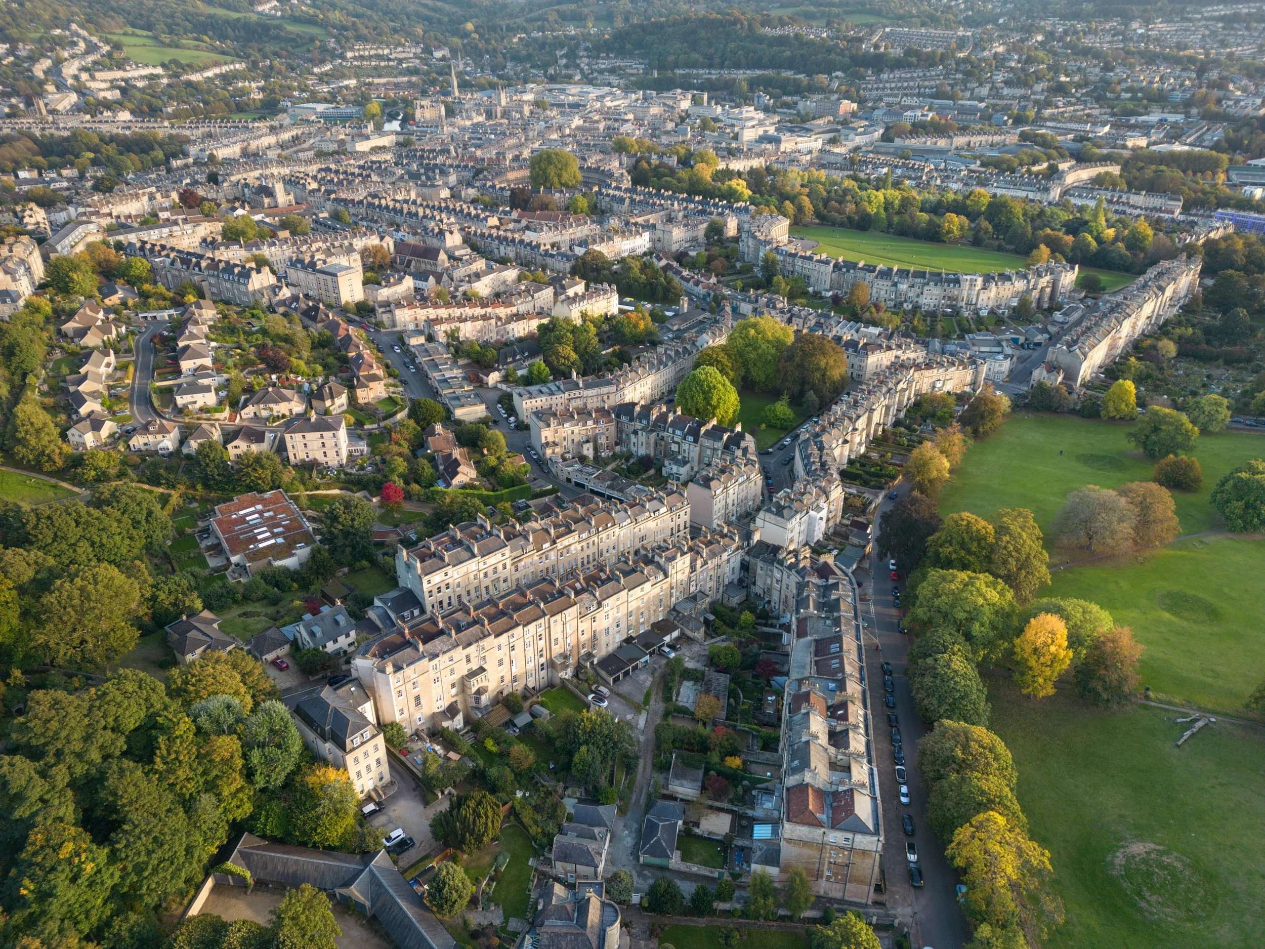 An aerial view of a cityscape with a mix of residential buildings, green parks, and tree-lined streets. The image captures a sprawling urban area with a variety of architectural styles and abundant greenery.