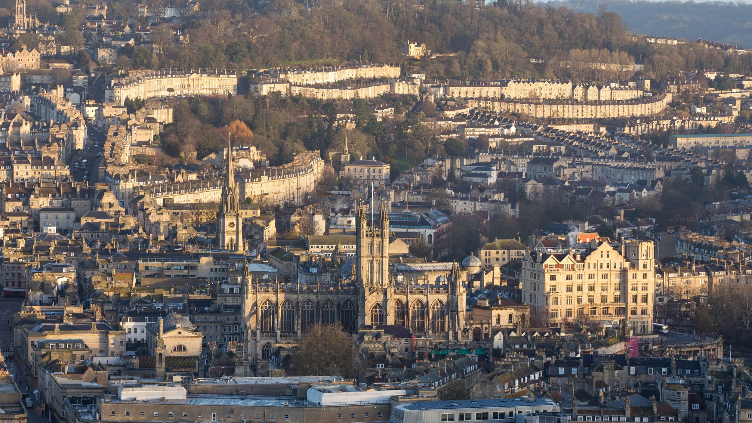 A panoramic view of a European city with historic and modern buildings, including a prominent Gothic-style cathedral with tall spires, surrounded by densely packed streets and houses, with hills in the background.