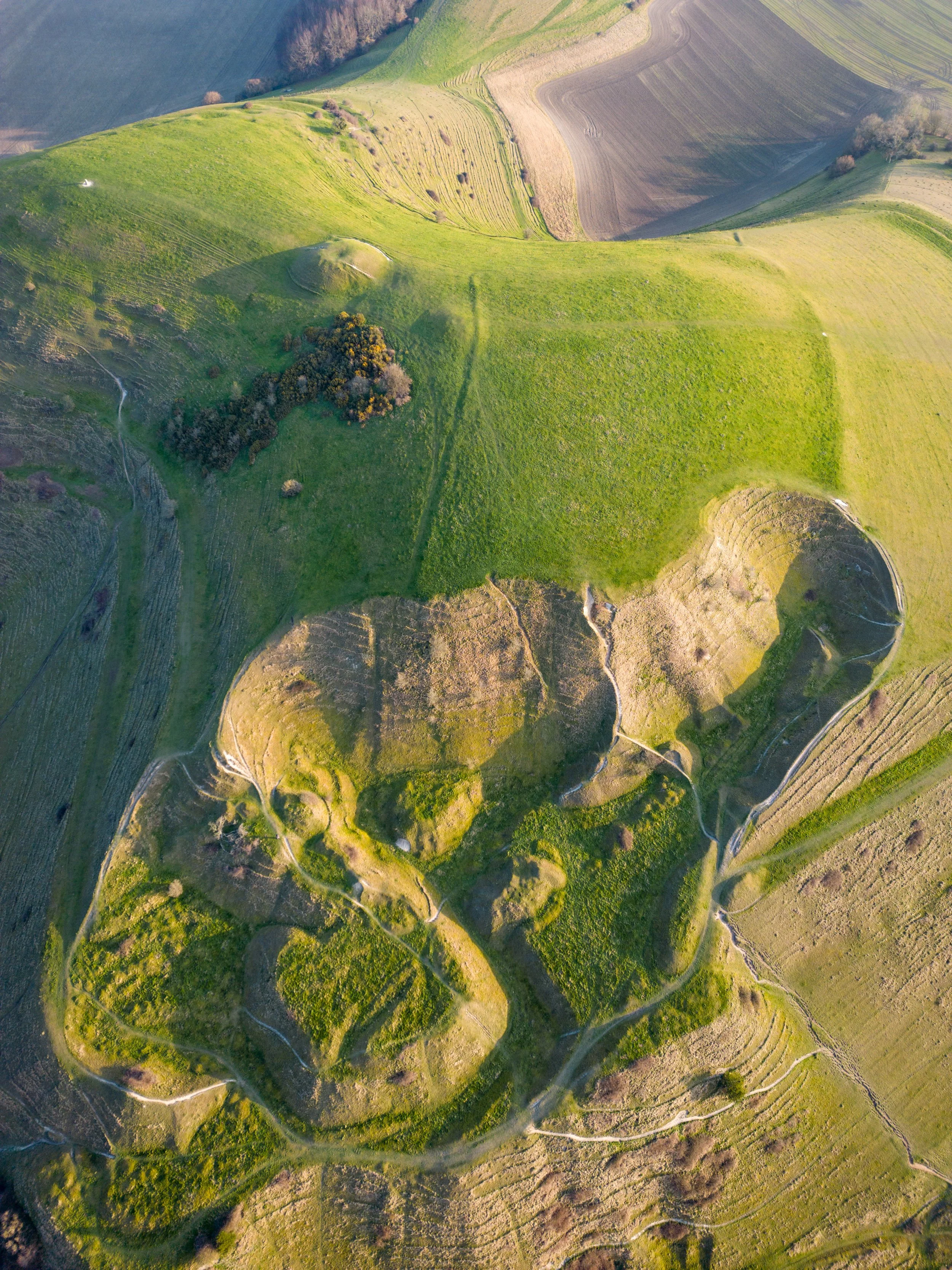 Aerial view of a green hilly landscape with pathways and patches of vegetation.