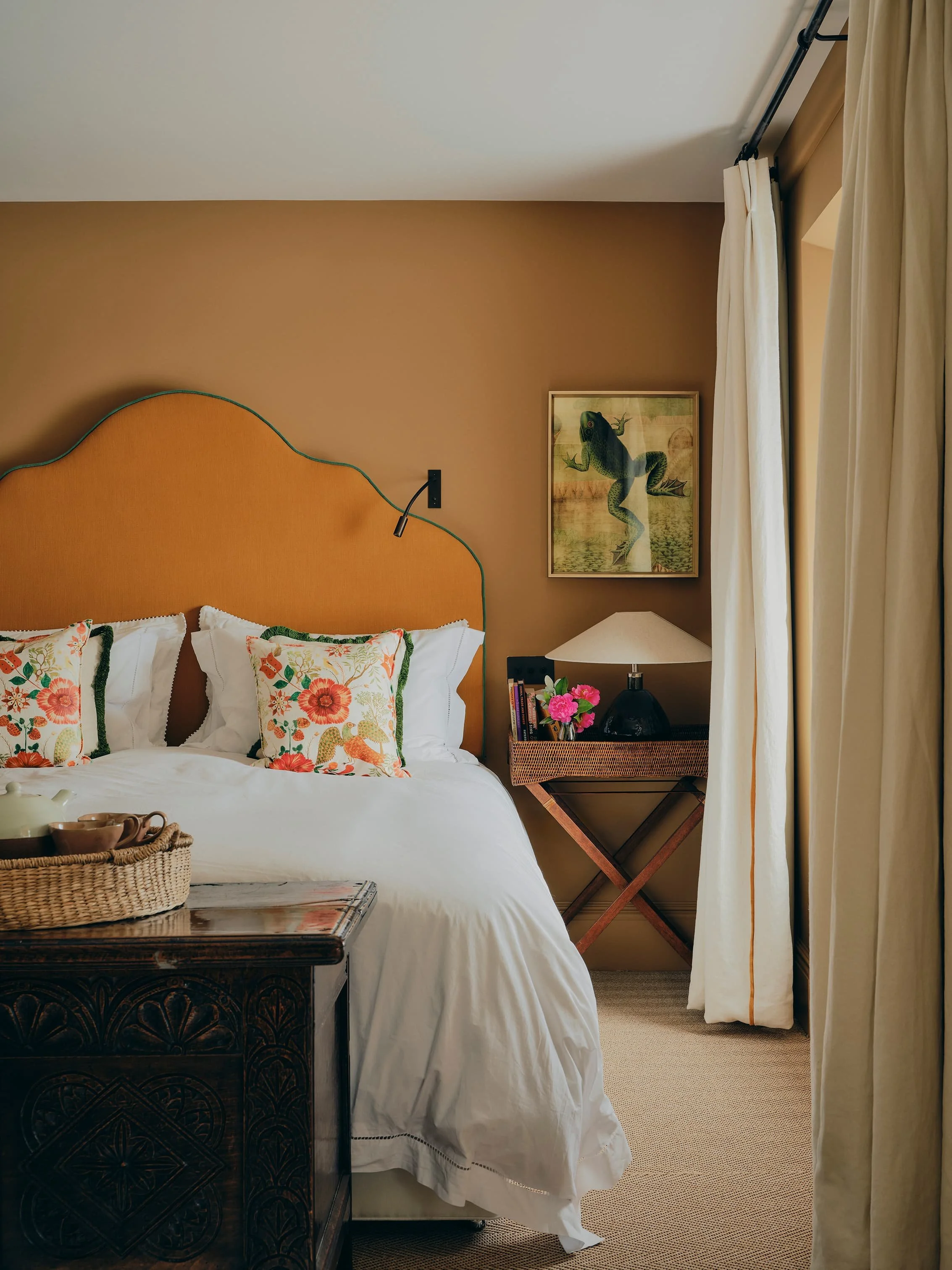 "Bedroom with curved orange headboard and floral cushions in a Jersey rural rectory by Bryony Richardson"