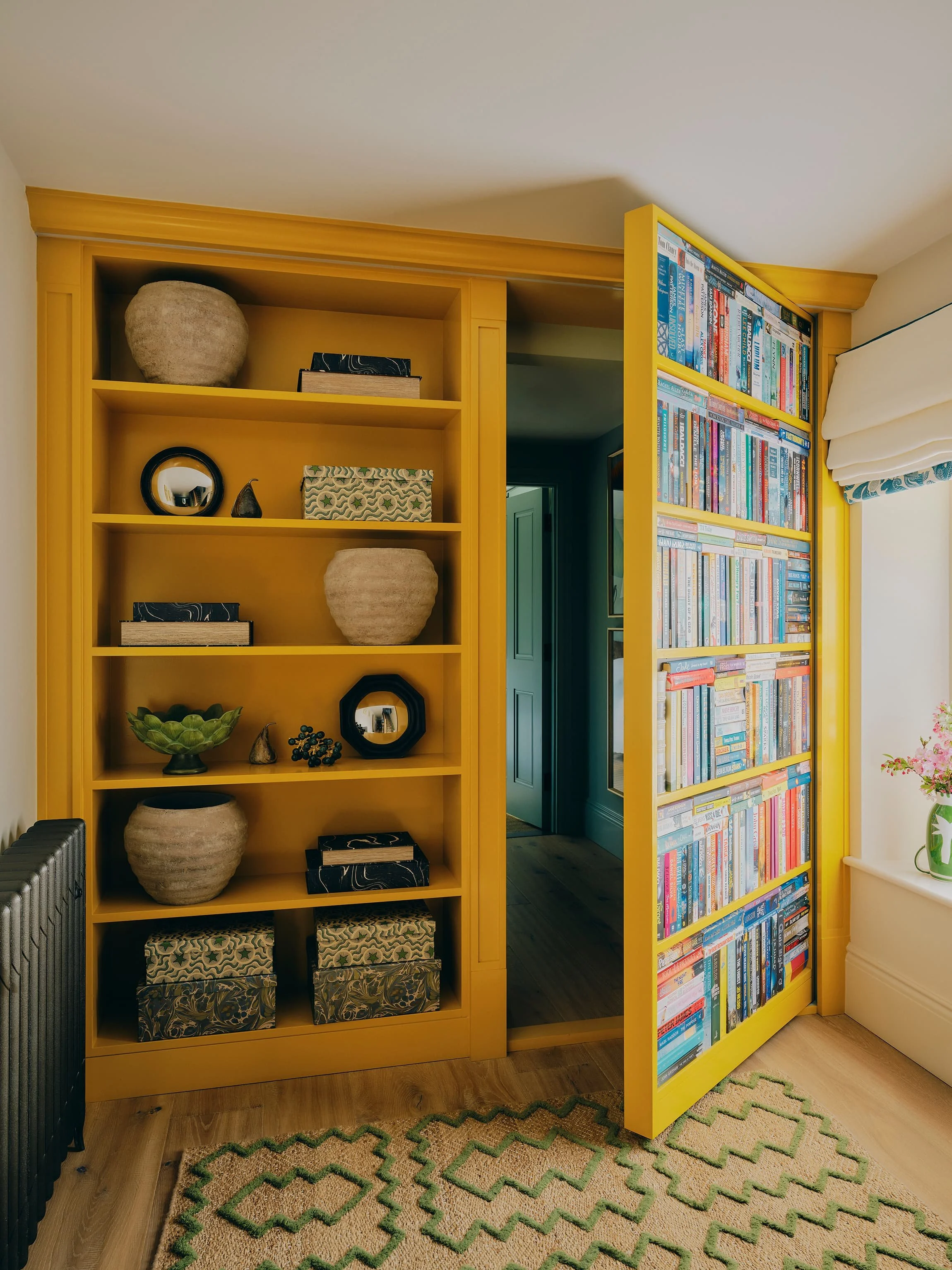 "Hidden bookcase door built into mustard yellow shelving in a Jersey rural rectory by Bryony Richardson"