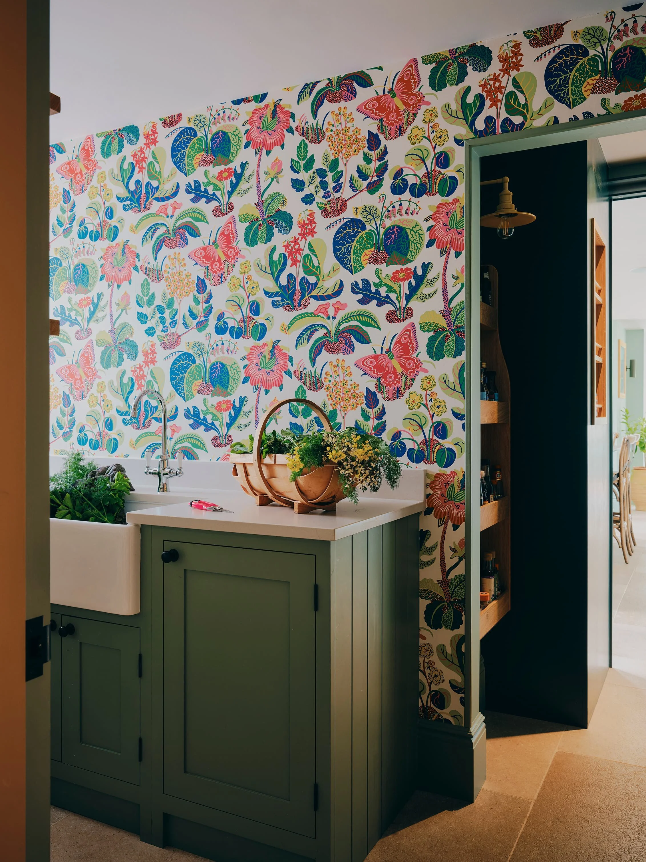 Utility room with bold floral wallpaper, green cabinetry, and Belfast sink in a Jersey rural rectory by Bryony Richardson