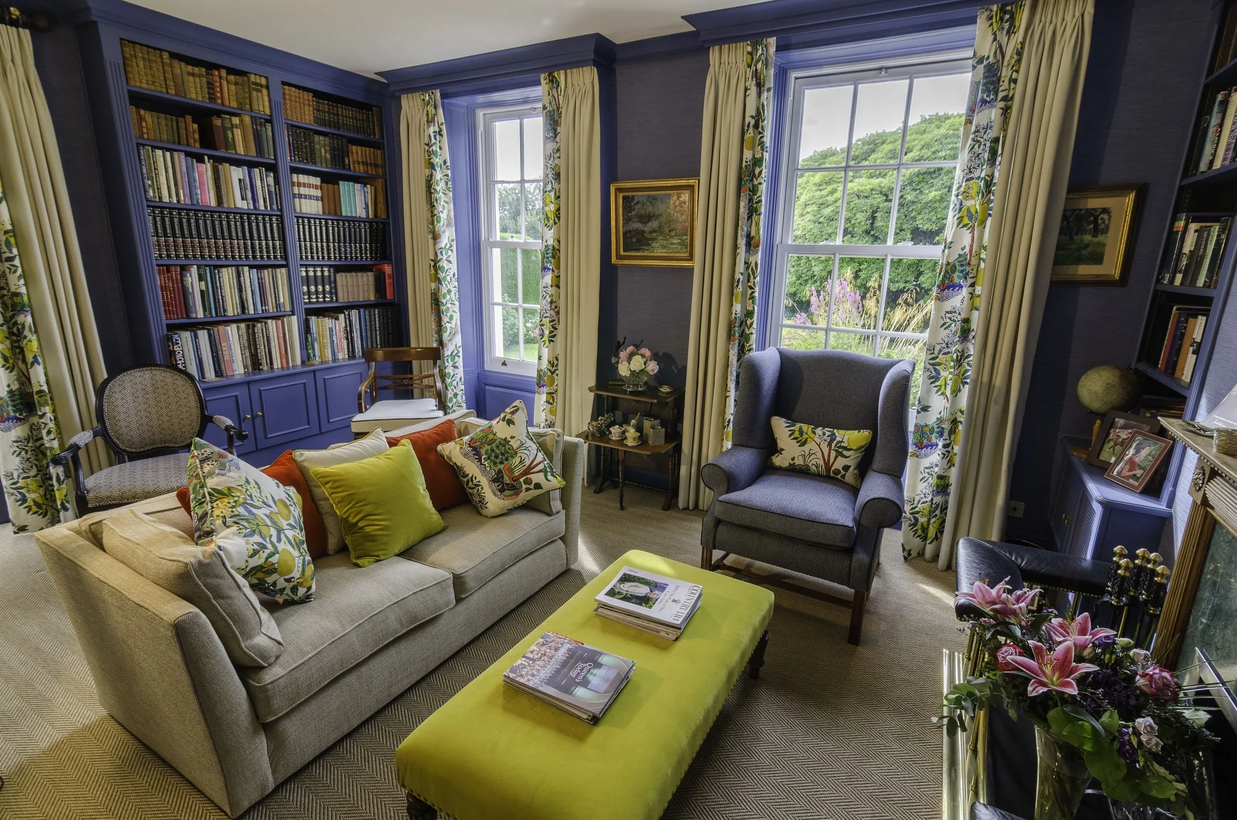"Blue drawing room with built-in bookshelves, floral curtains and colourful cushions in a St Lawrence, Jersey country house, designed by Bryony Richardson"