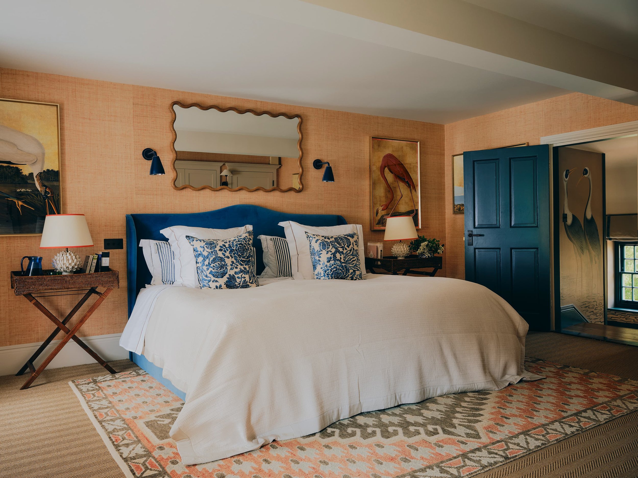 Bedroom with navy velvet headboard, scalloped mirror, and flamingo artwork in a Jersey rural rectory by Bryony Richardson