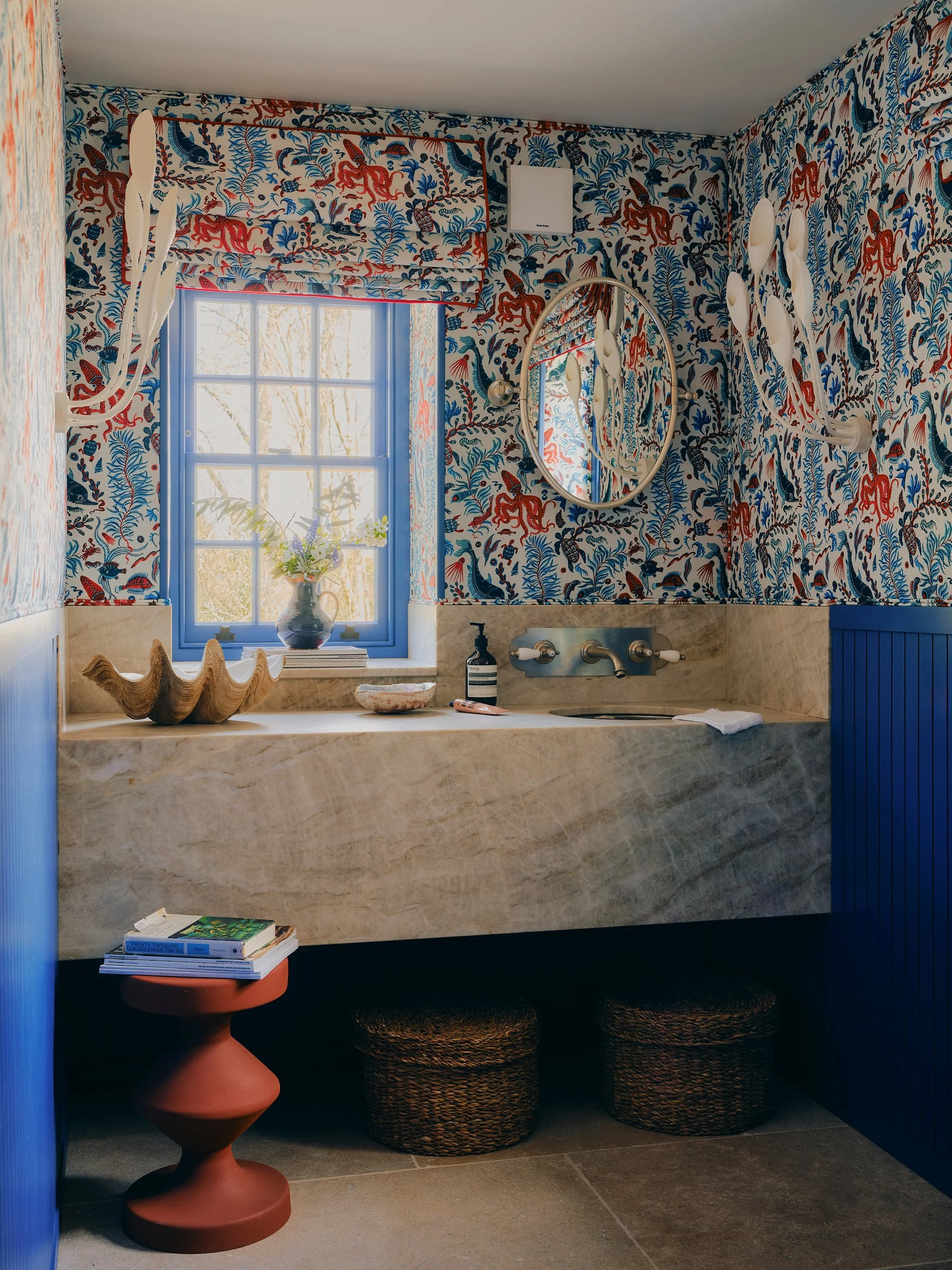 Cloakroom with bold aquatic-themed fanny shorter fabric wallpaper, floating marble vanity, organic plaster lights and hammered bronze sink in a Jersey rural rectory by Bryony Richardson