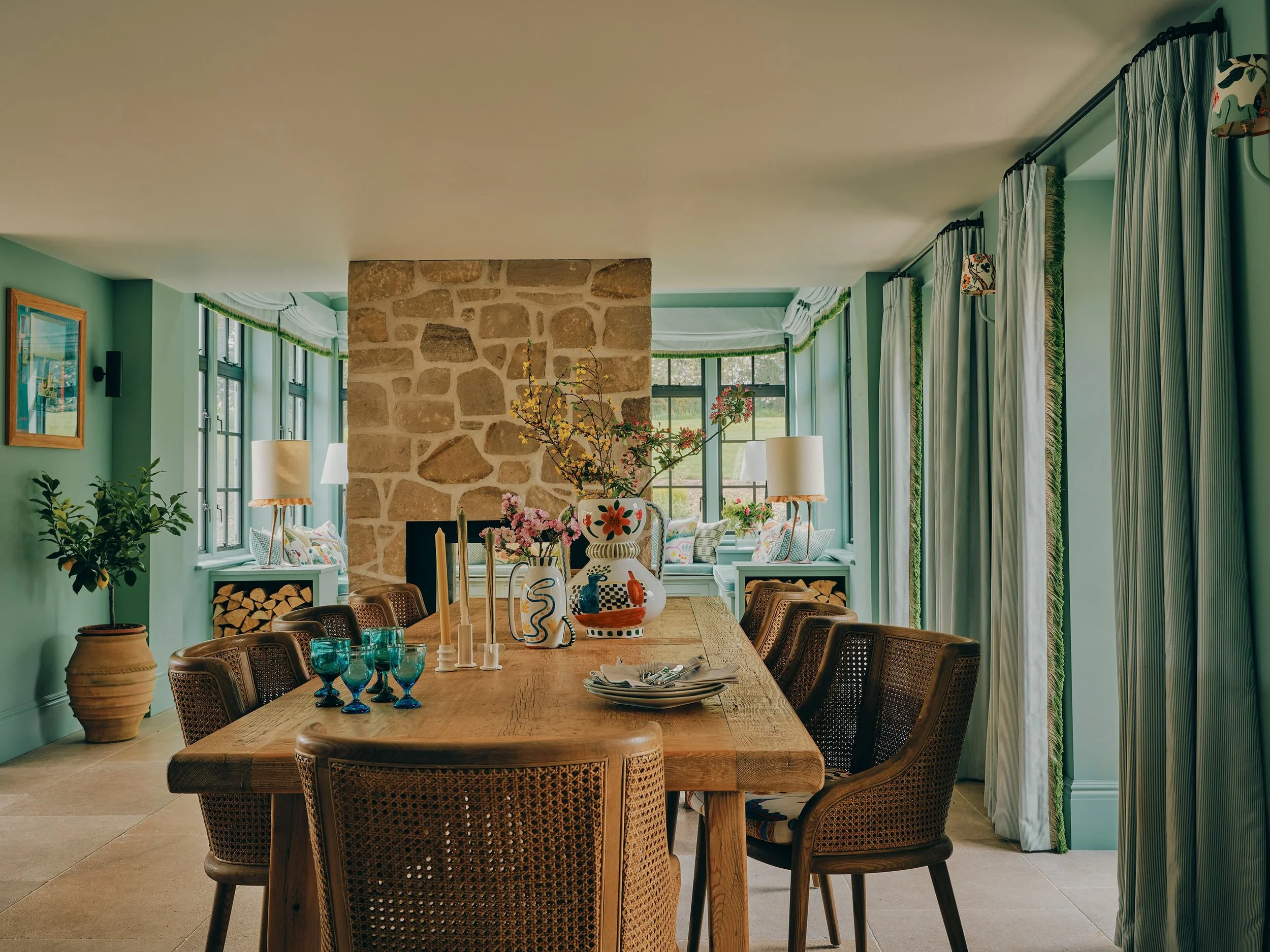 "Dining room with reclaimed wood table, stone fireplace, and cane chairs in a Jersey rural rectory by Bryony Richardson"