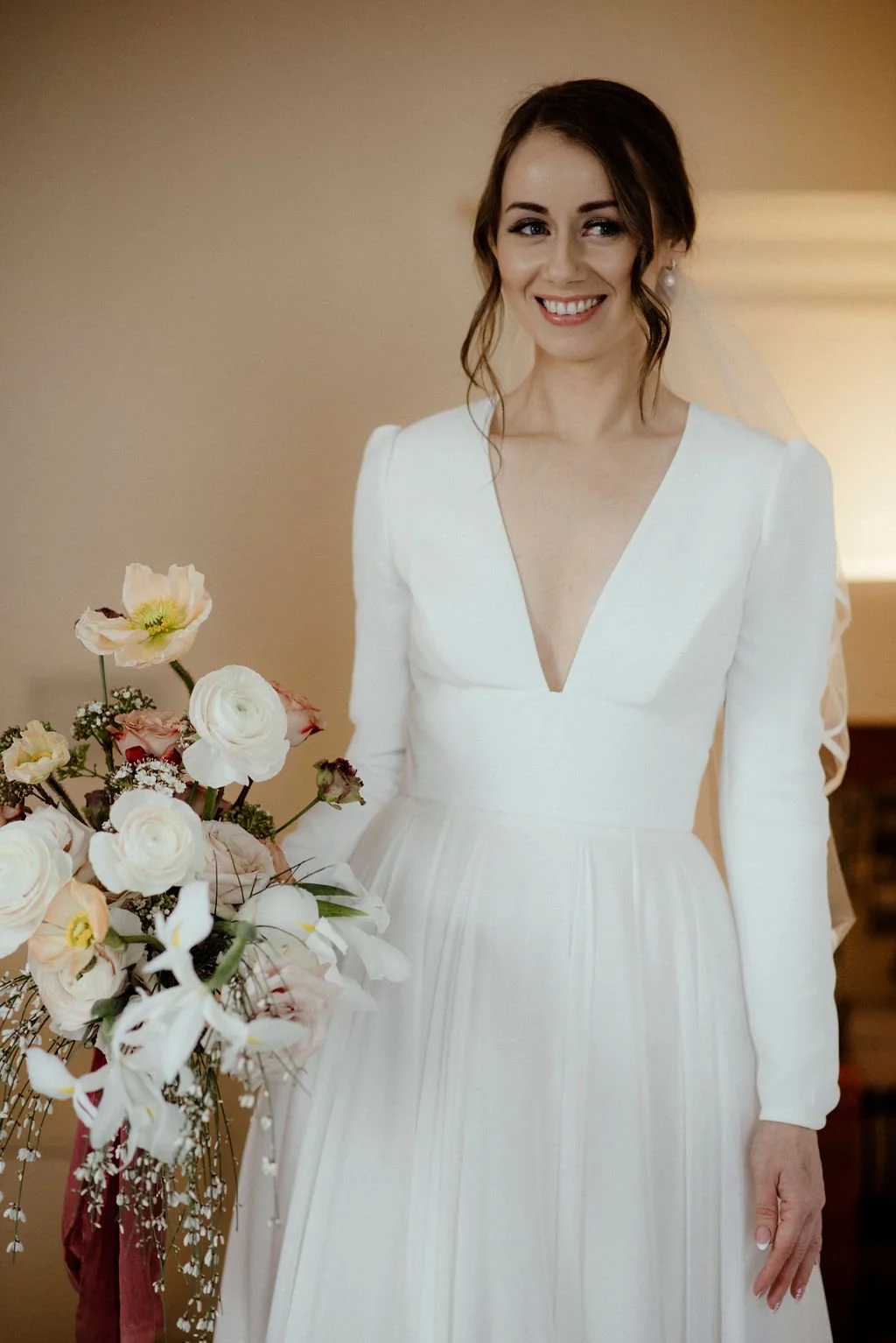 A woman in a white wedding dress smiling next to a bouquet of flowers.