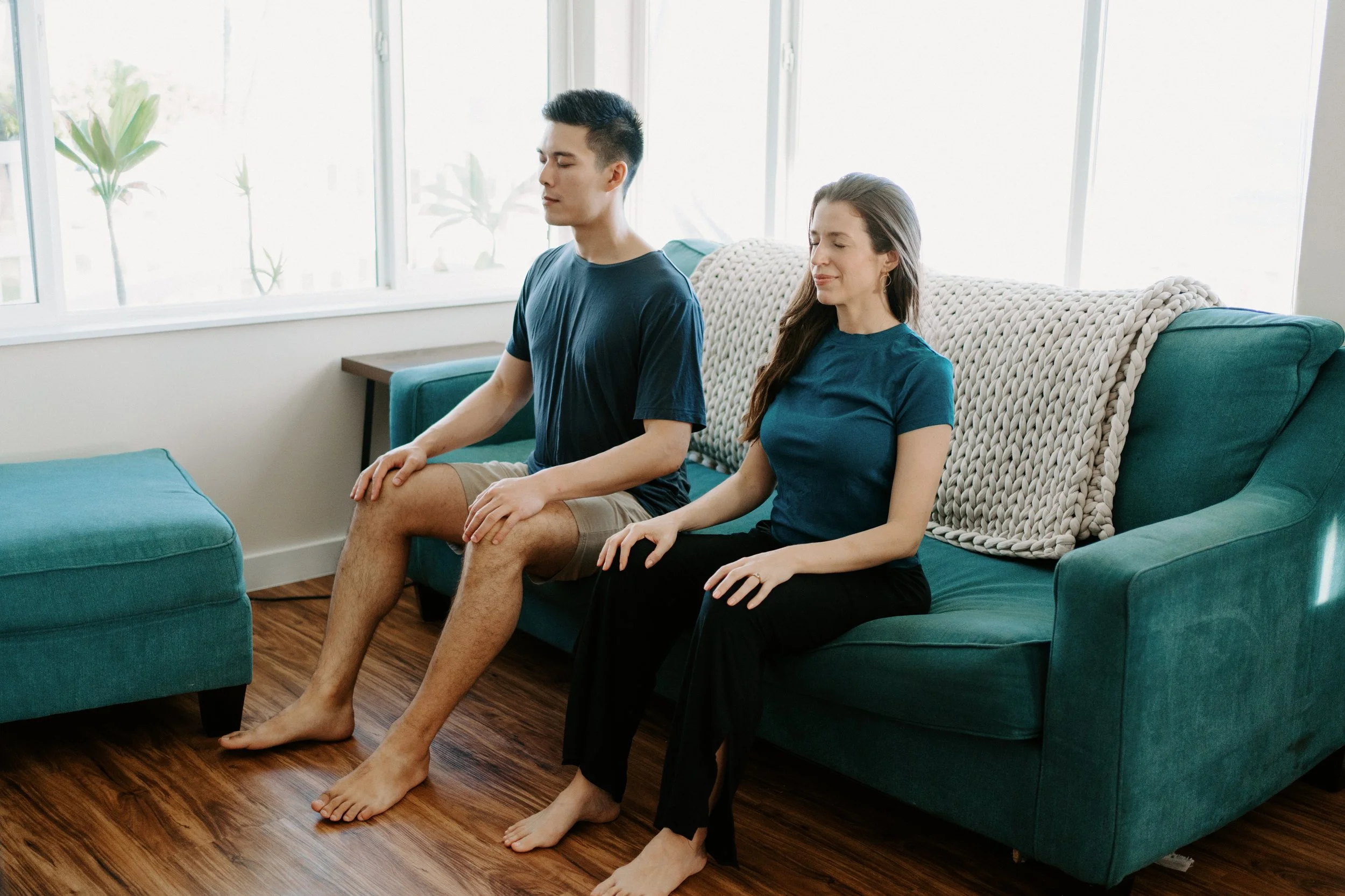 Ann and her husband sitting on a couch, meditating with eyes closed and hands resting on their legs.