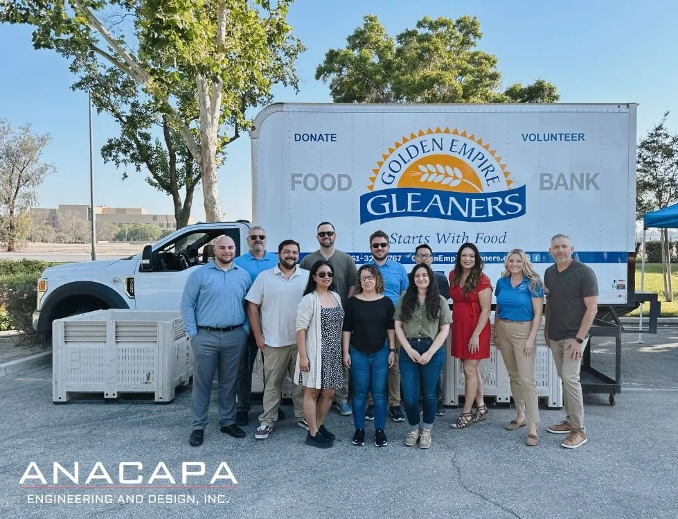 A group of Anacapa staff standing in front of a Golden Empire Gleaners food bank truck, with "Anacapa Engineering and Design, Inc." logo in the bottom left corner.