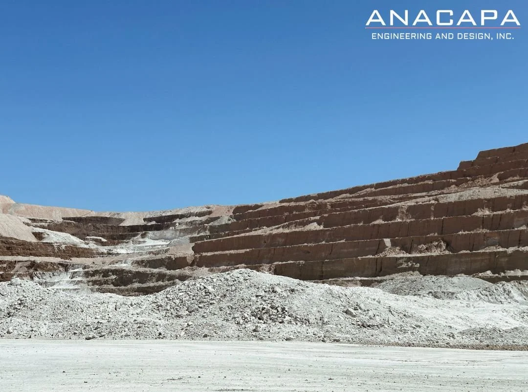 A terraced rock quarry with multiple levels and debris in the foreground, under a clear blue sky. The words "ANACAPA ENGINEERING AND DESIGN, INC." are written in the top right corner.