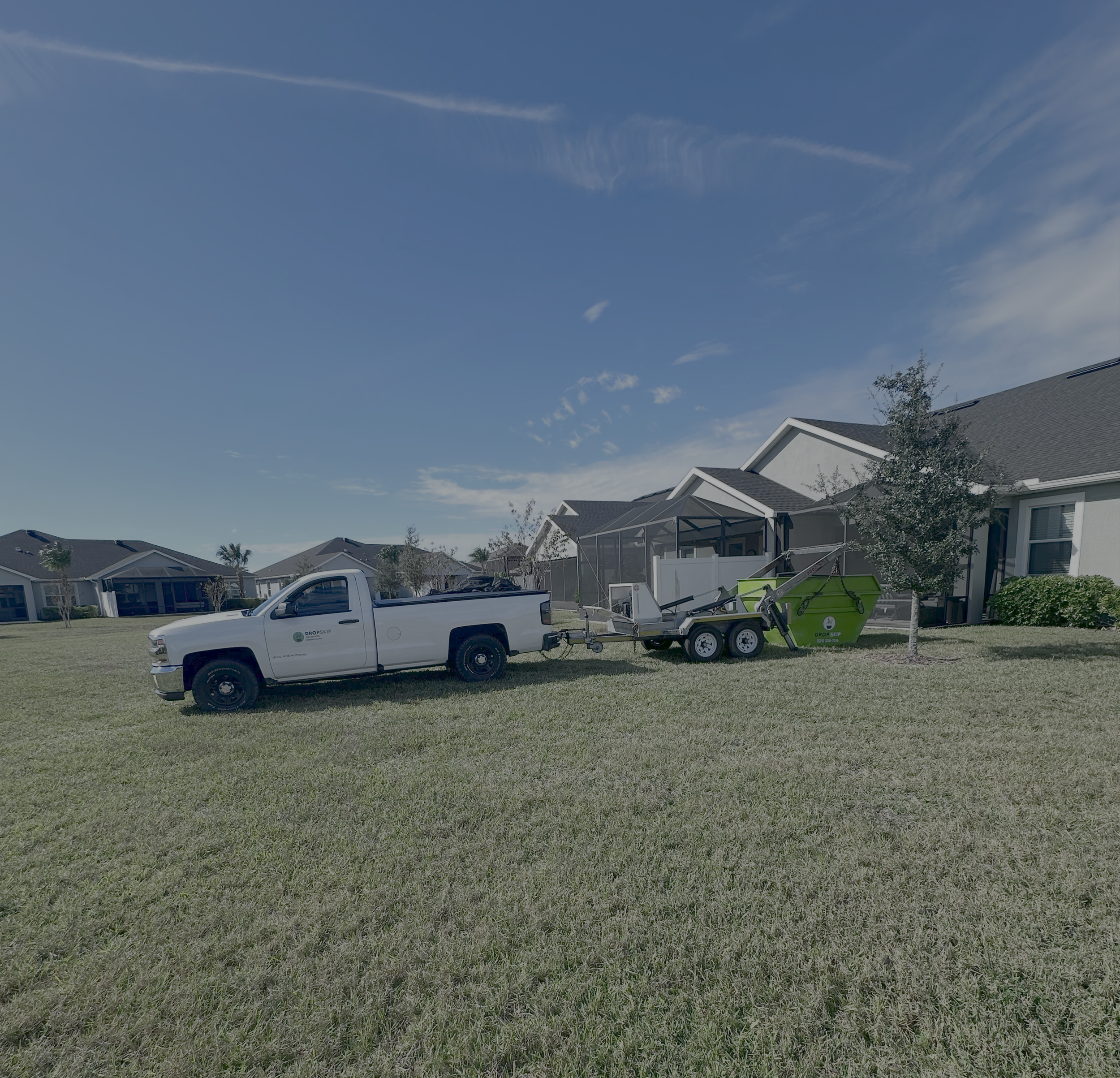 Pickup truck pulling a trailer with yard equipment beside a house with a screened porch on a grassy lawn