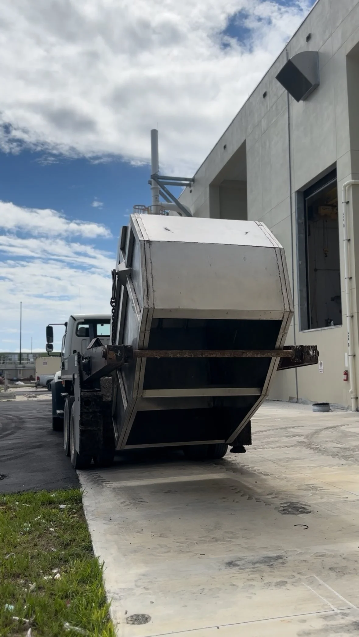 A dump truck with a raised bed parked on a driveway next to a building.