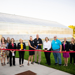 Group of community leaders cutting red ribbon outside greenhouse