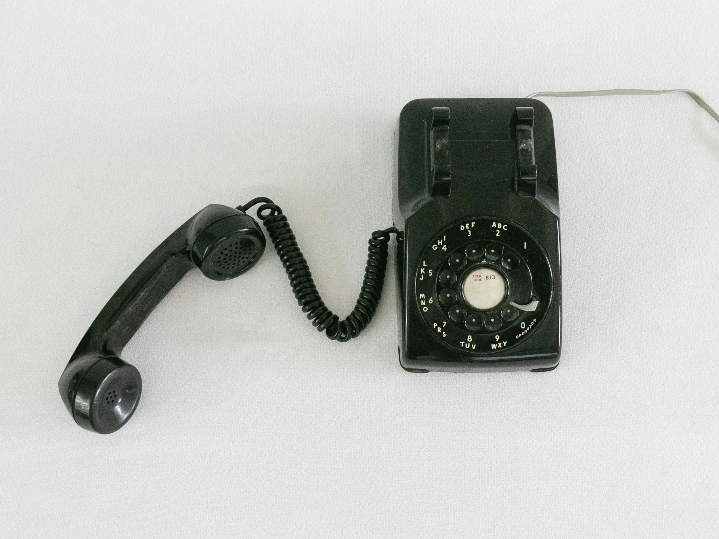 Vintage black rotary dial telephone with a cord on a white surface.