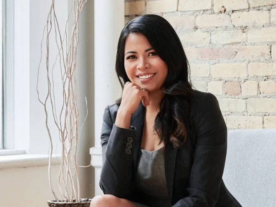 Admin Assistant for the top financial planners winnipeg  Mignon North sitting casually in a green dress on a black leather chair smiling and pulling her hair behind her ear.