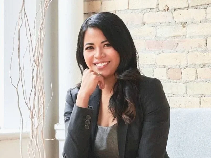Admin Assistant for the top financial planners winnipeg  Mignon North sitting casually in a green dress on a black leather chair smiling and pulling her hair behind her ear.