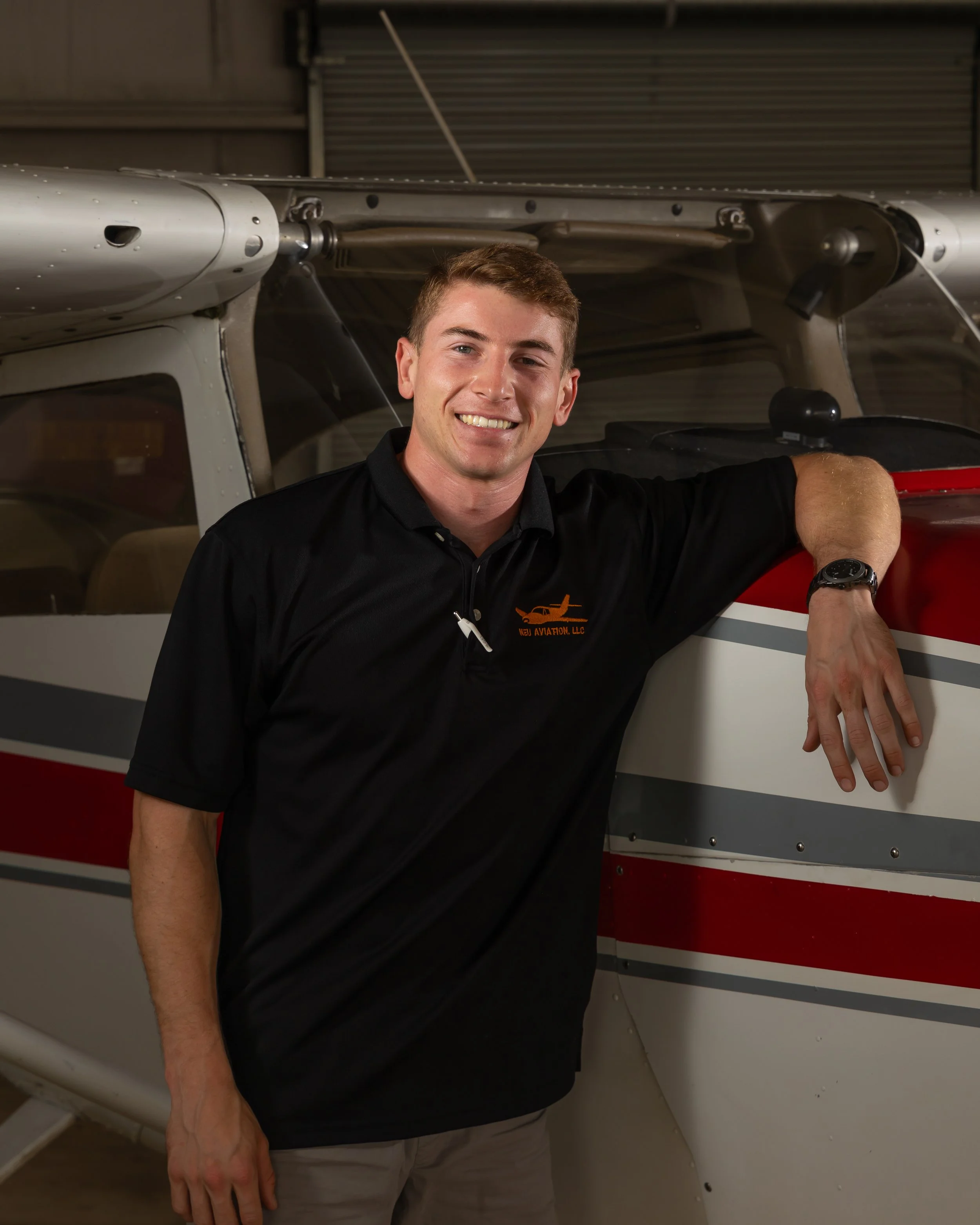 Smiling man wearing a blue polo shirt with an NEX Aviation logo, standing against a brown background.