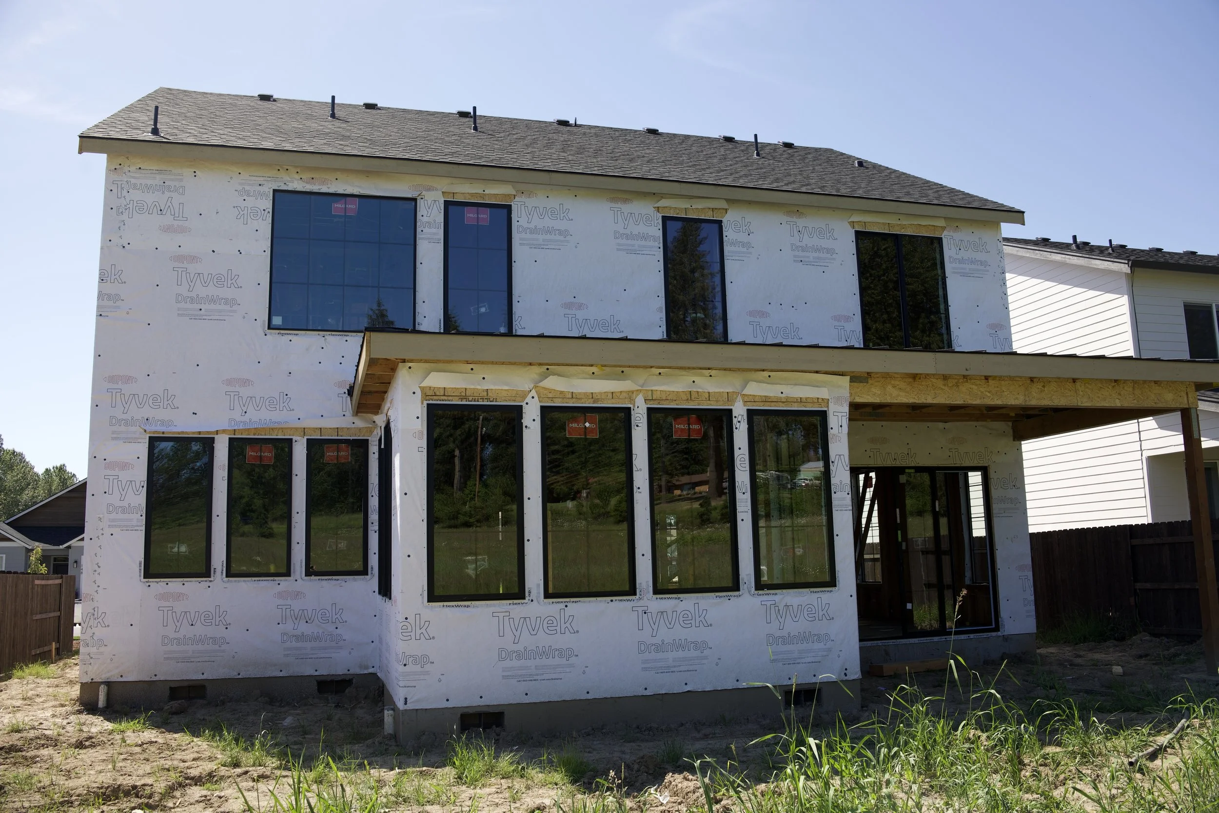 Modern custom home under construction featuring large black framed windows, covered outdoor patio, and contemporary residential architecture in Washington.