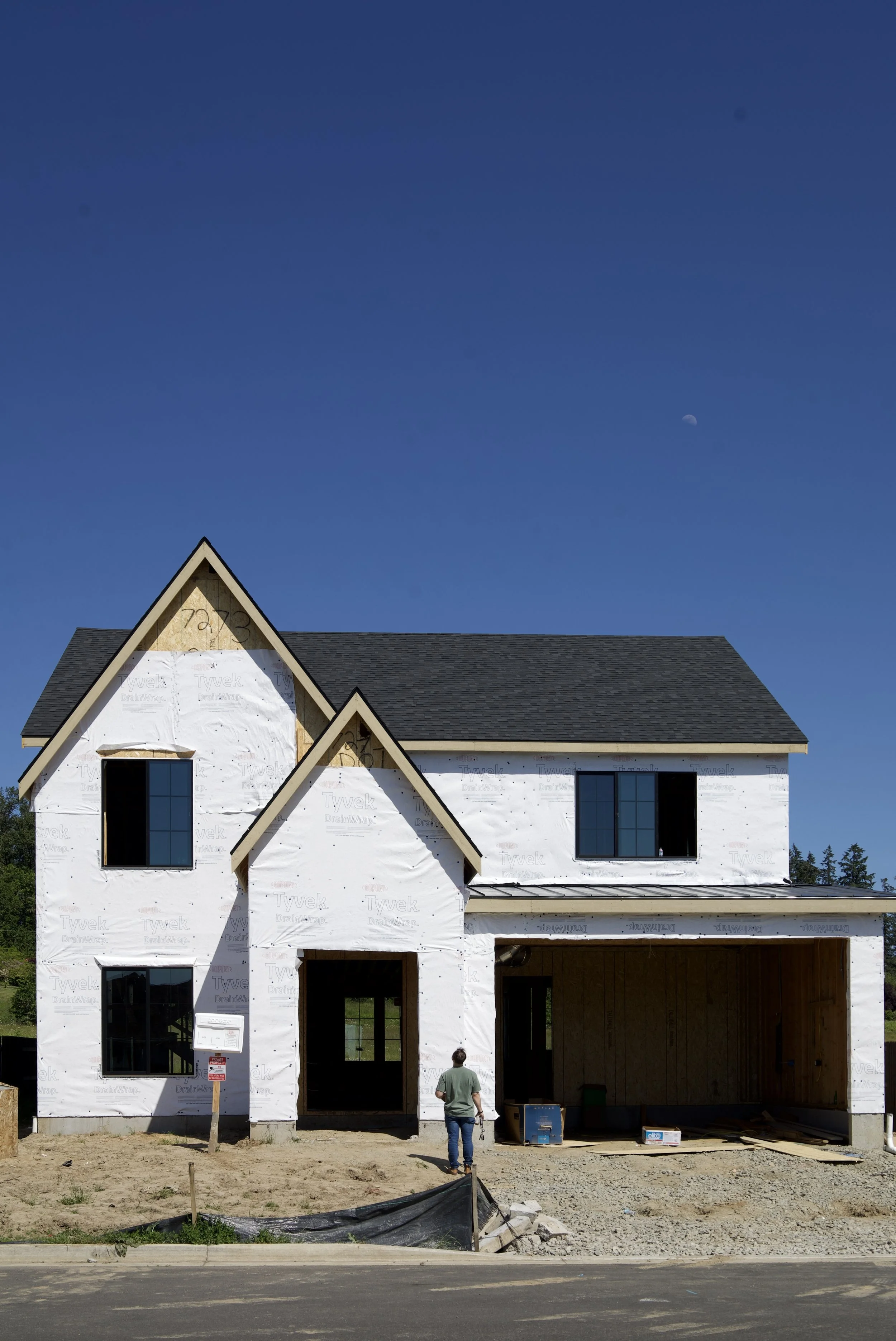 Front elevation of a modern farmhouse style custom home under construction with steep gable rooflines, covered entry, and attached garage in LA Center,Washington.