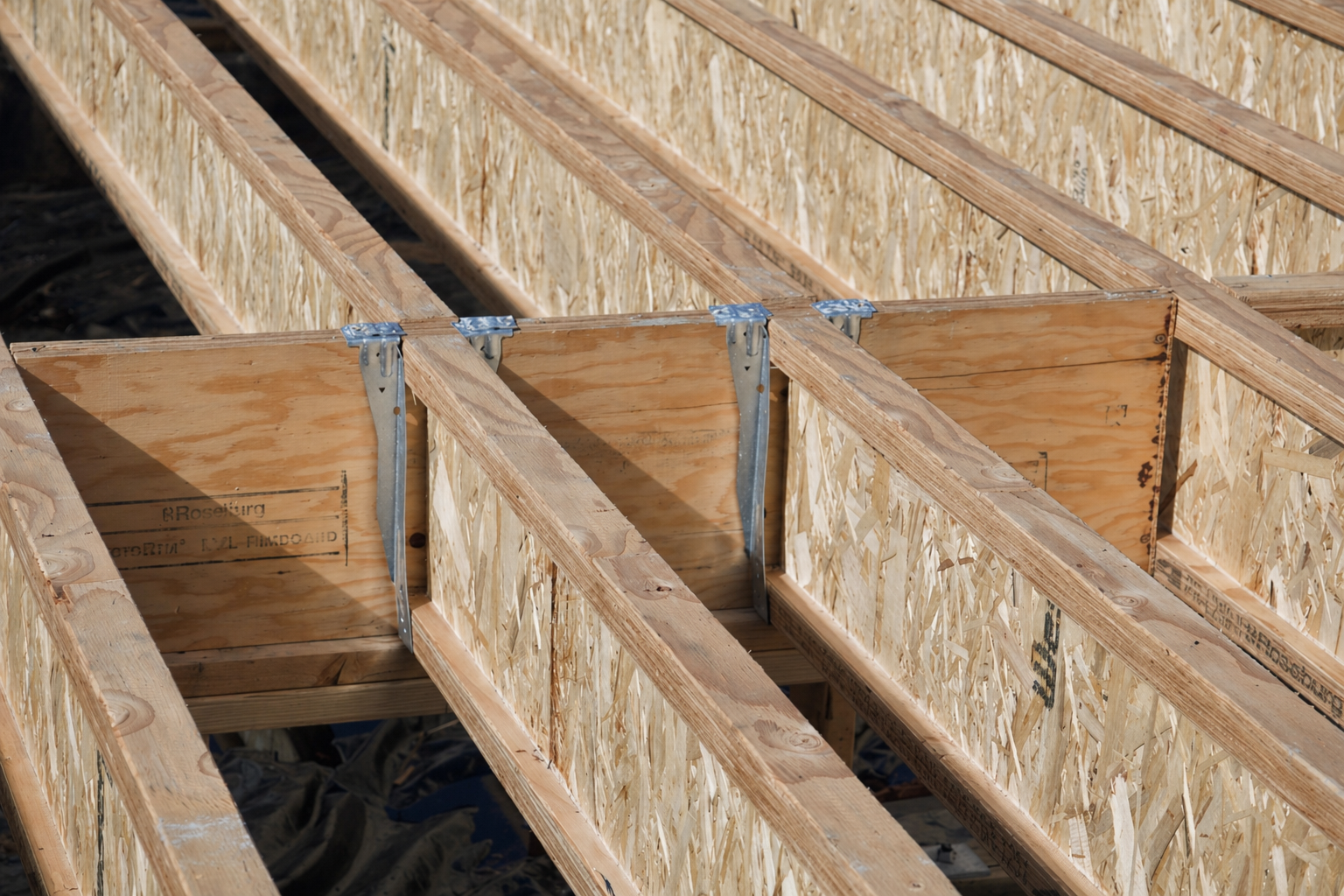 Close-up of engineered wood floor joists with metal joist hangers during custom home construction by Anthropos Design.