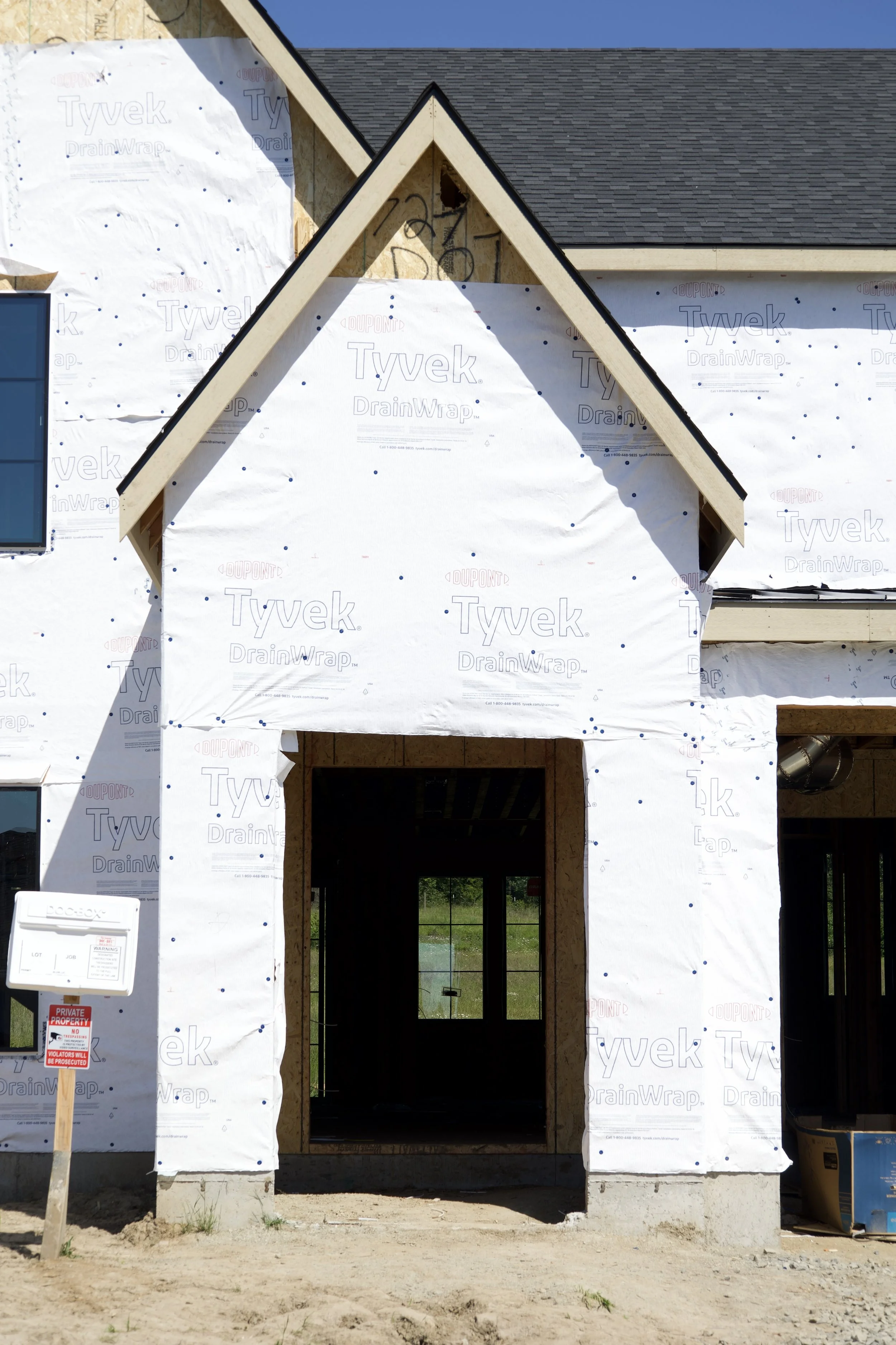 Close-up of modern custom home front entry with gabled porch detail, natural wood trim, and contemporary residential architecture under construction.