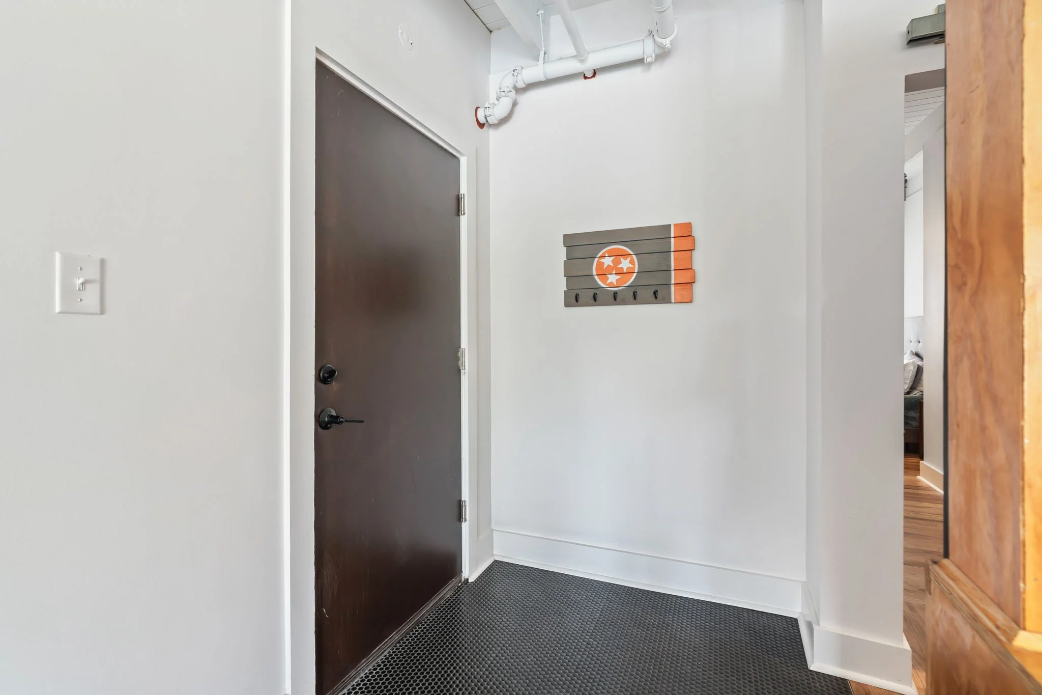 An entryway with a dark brown door, white walls, a black textured floor mat, and a wall-mounted wooden decorative piece with the Tennessee state emblem.
