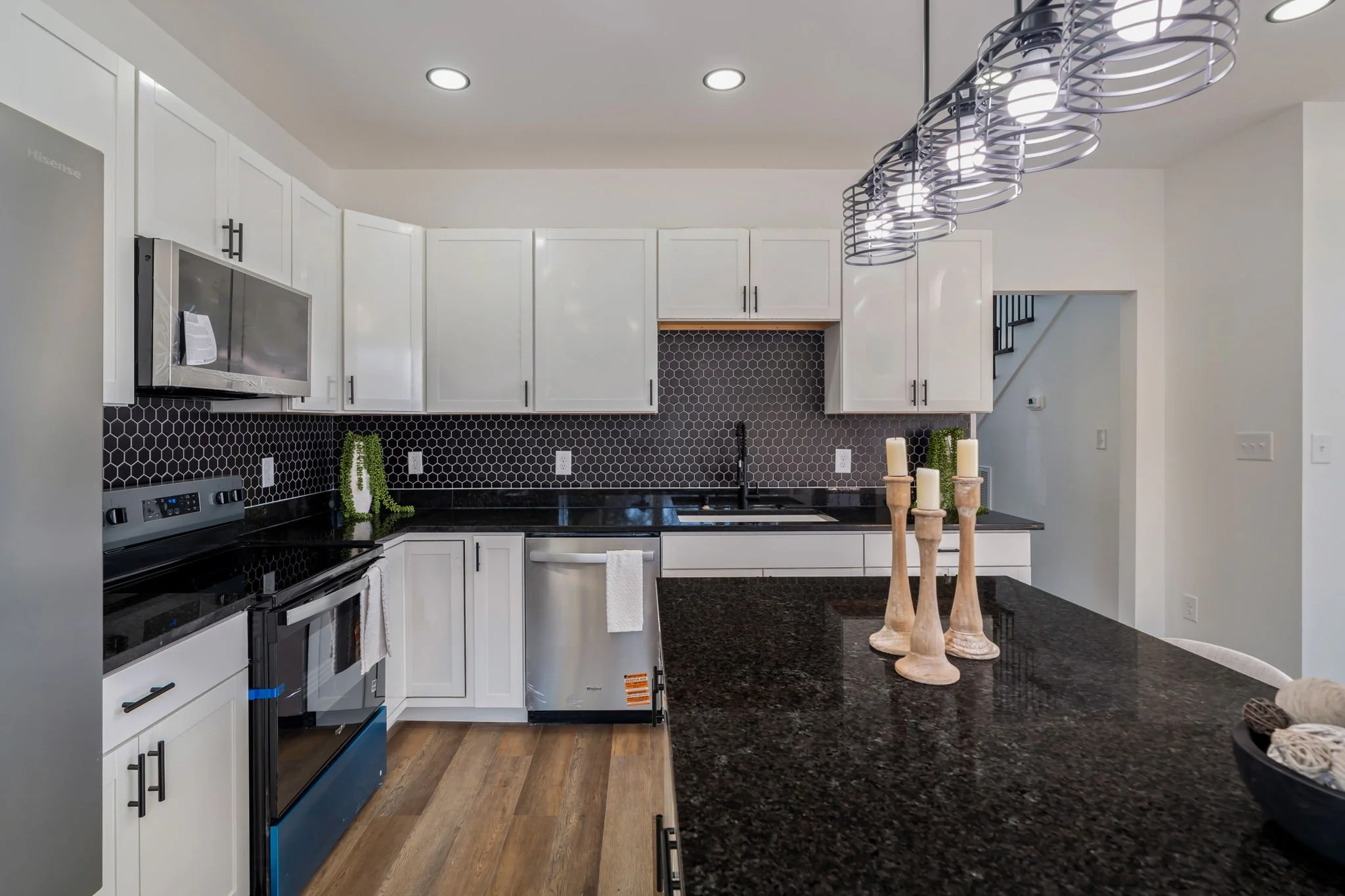 Modern kitchen with white cabinets, black countertops, hexagonal black backsplash, stainless steel appliances, and a black island with three beige candle holders.