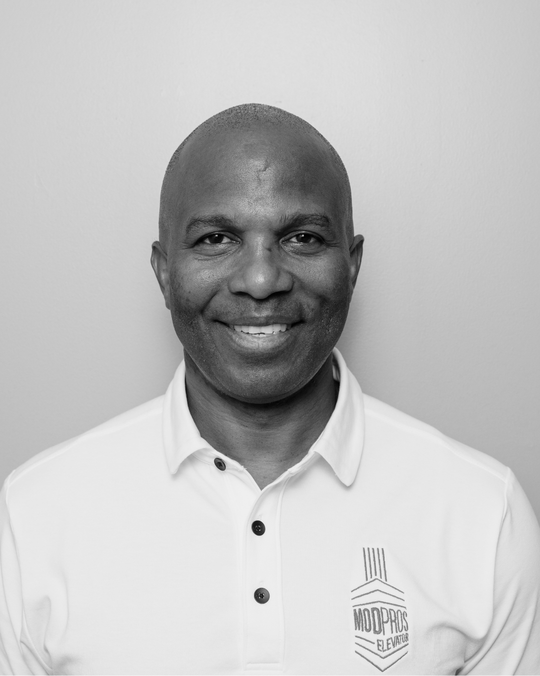 Black and white portrait of a smiling man wearing a collared shirt with a logo that reads 'MODPROS Elevator'.