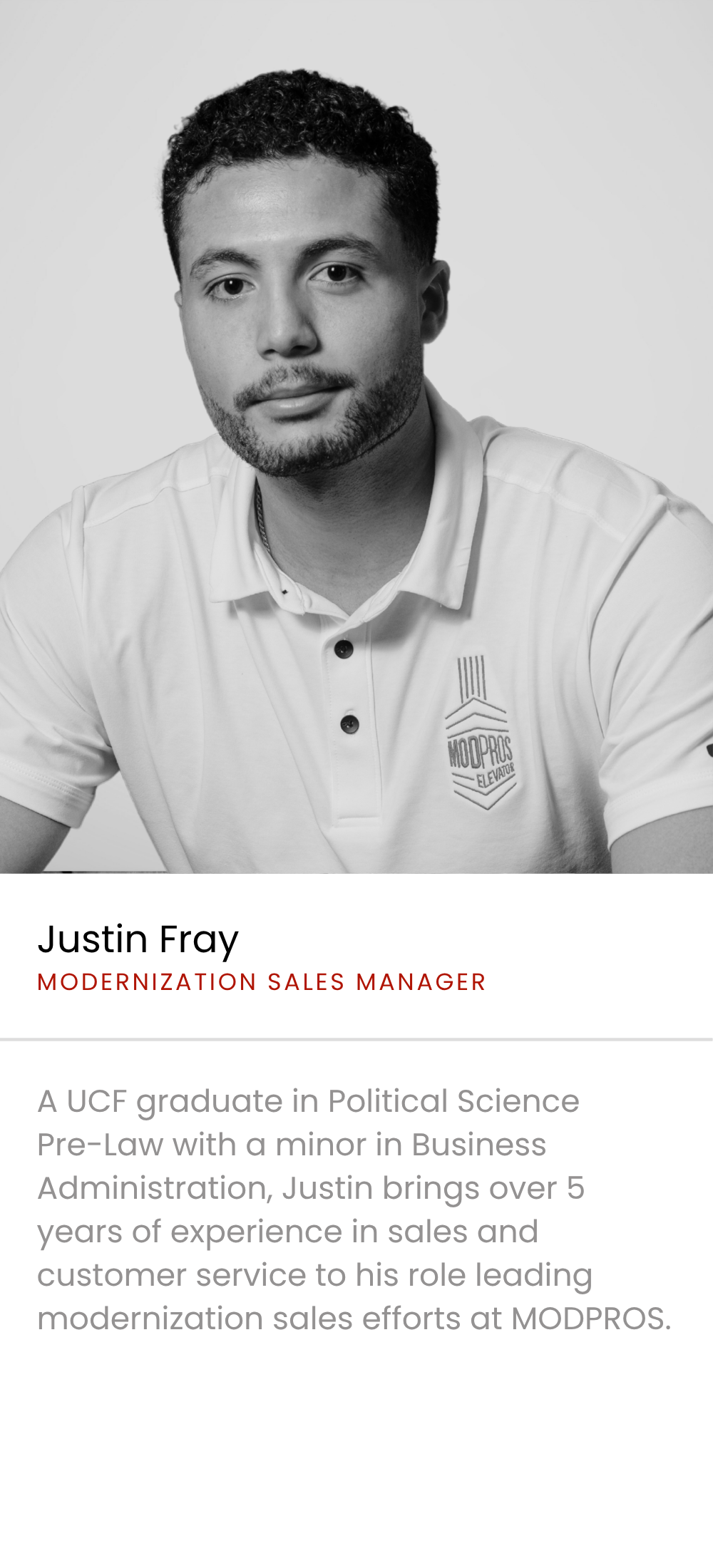 Black and white portrait of Justin Fray, a man with short curly hair, beard, wearing a polo shirt with a 'MODPROS ELEVATOR' logo, looking at the camera.