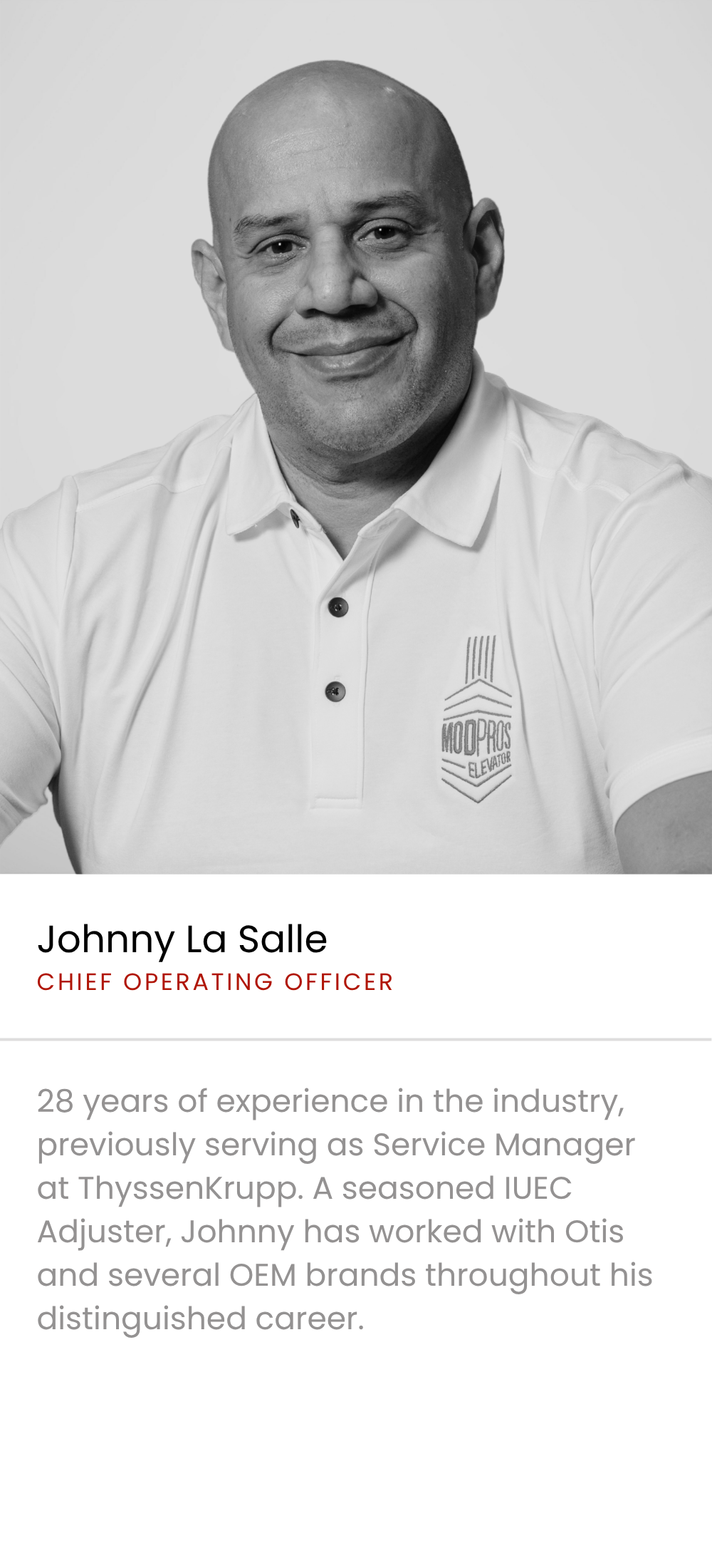 Black and white professional portrait of Johnny La Salle, a man with a bald head, smiling, wearing a polo shirt with the MOD PROS ELEVATOR logo, against a plain light background.