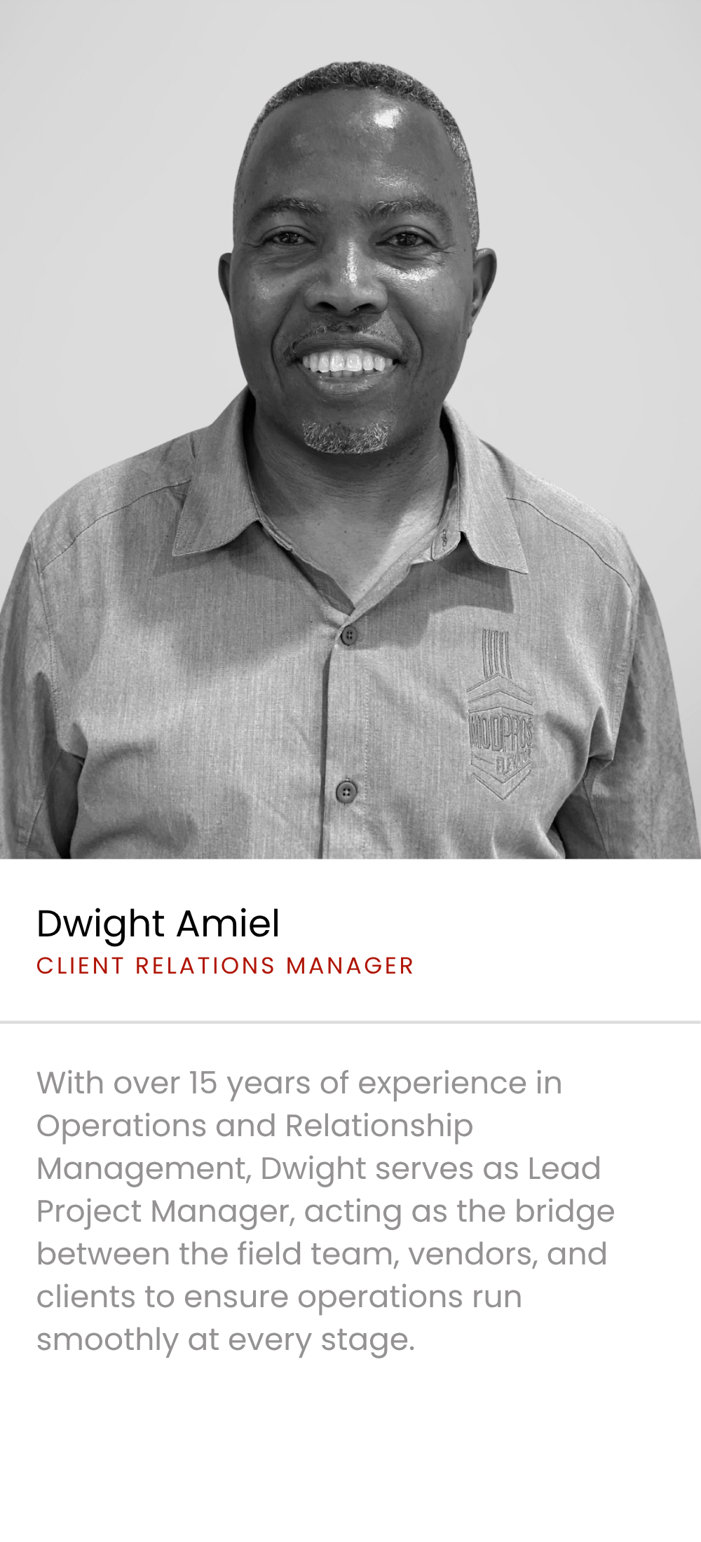 Portrait of Dwight Amiel, a Black man with short hair and a goatee, smiling, wearing a collared shirt with a company logo, against a plain background.