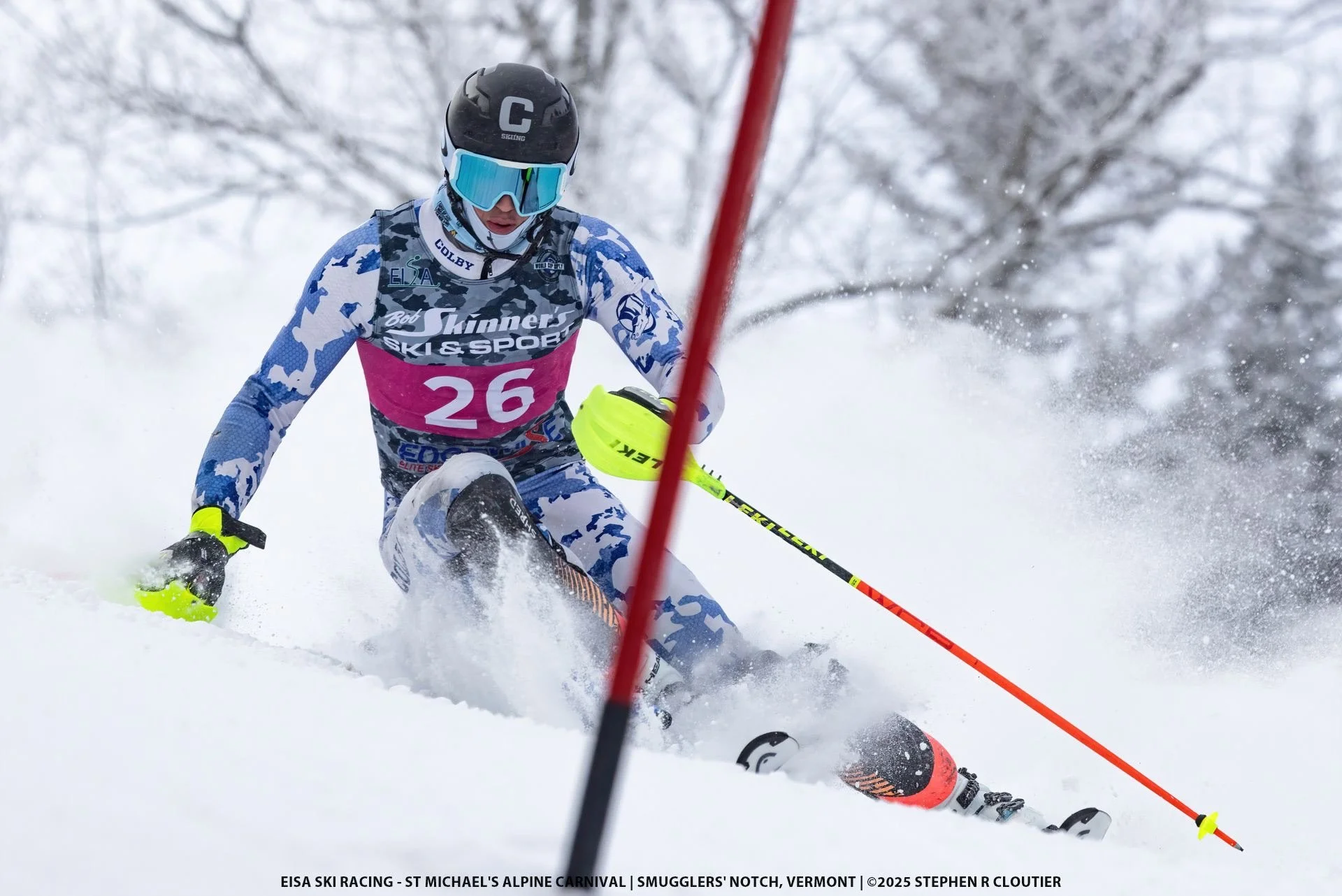 A skier in race gear skillfully navigating through a slalom course on snowy terrain, with a backdrop of snow-covered trees, during a competitive alpine skiing event.