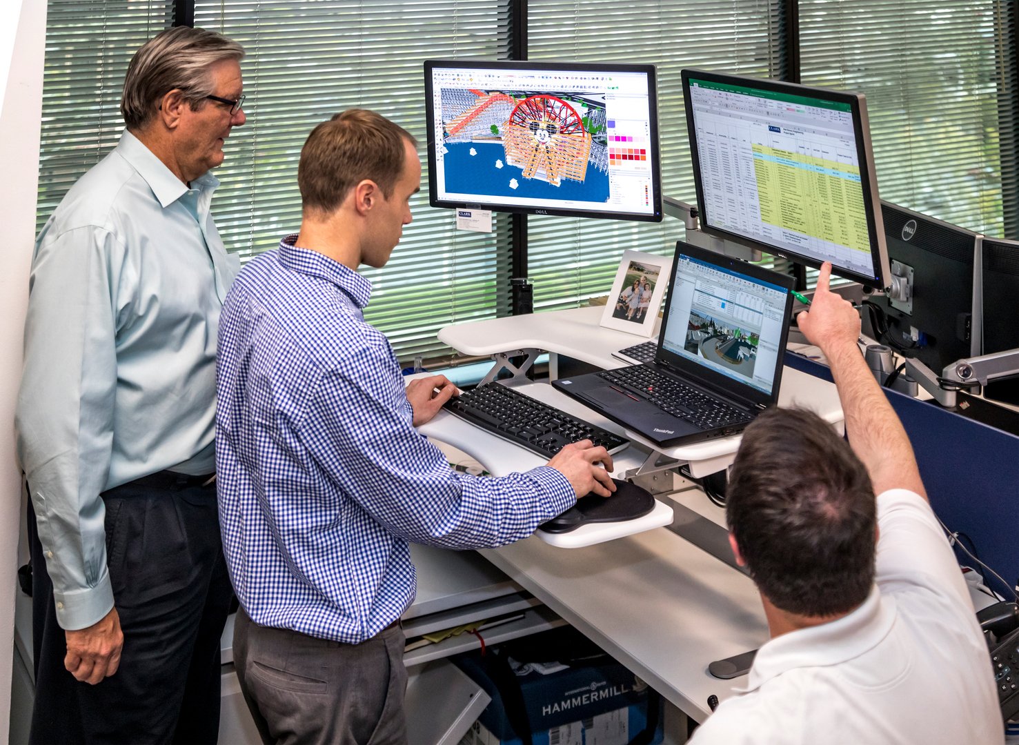 Four men working in an office with multiple computer monitors displaying technical and data projects.