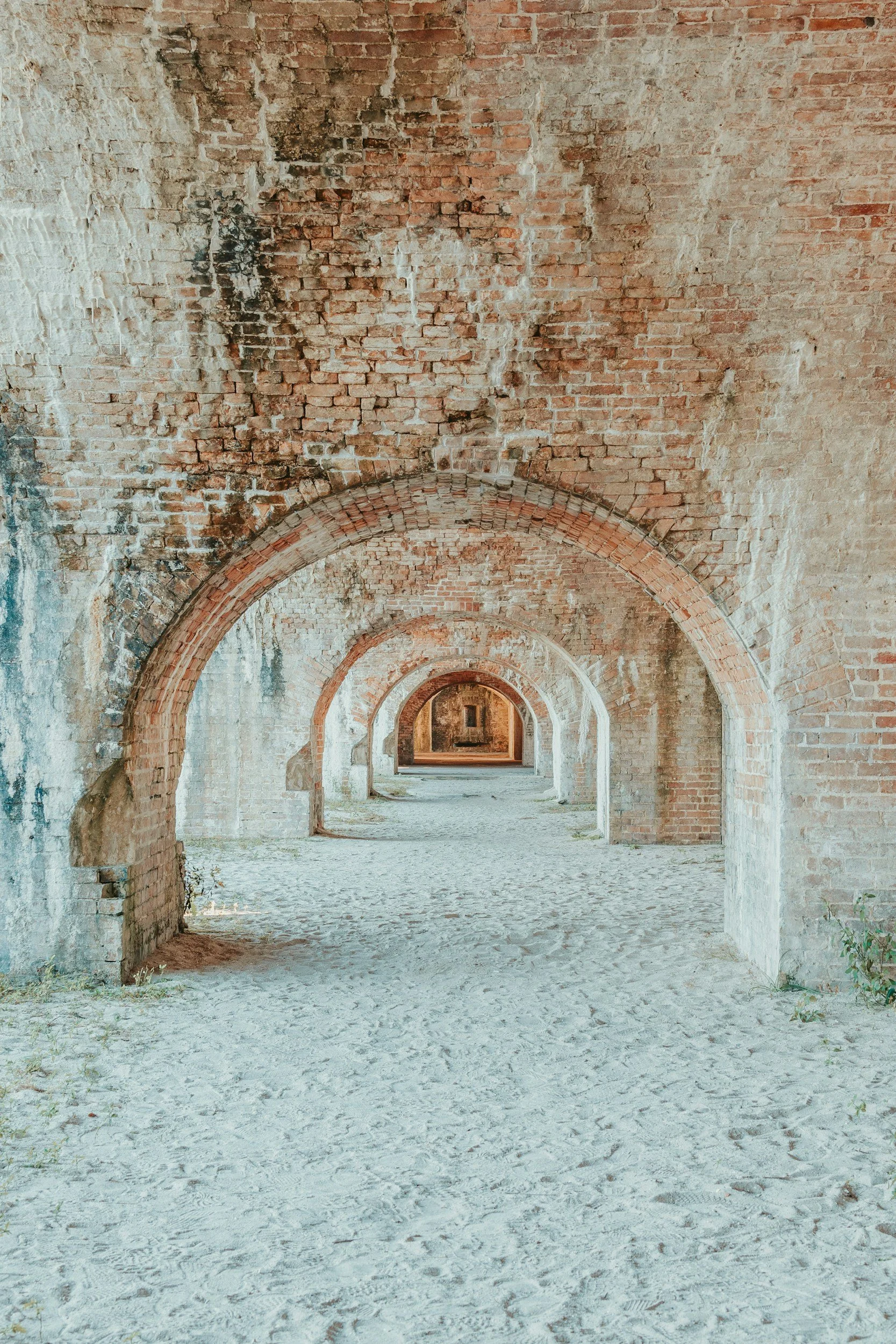 Series of brick arches in a historical structure with sandy ground and partially eroded brick walls.