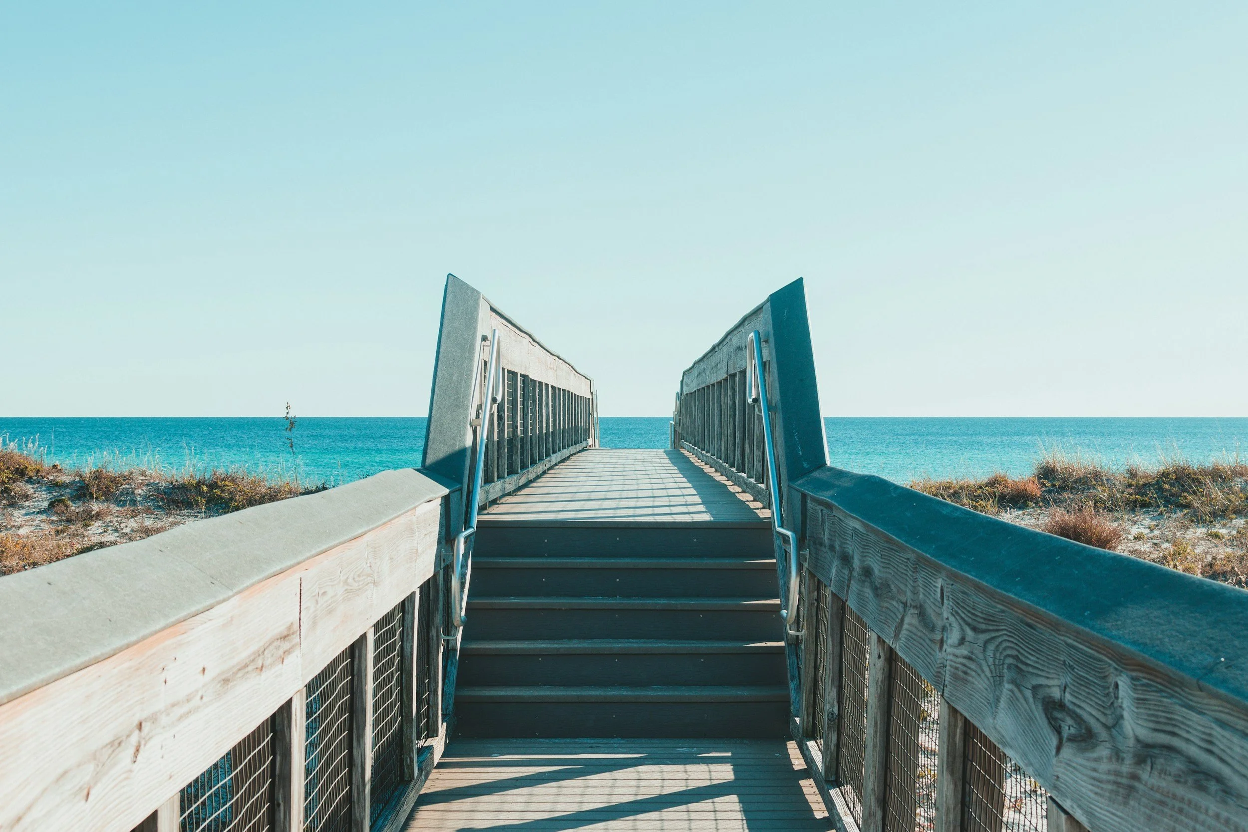 Wooden beach access ramp leading to sandy beach and ocean, clear blue sky