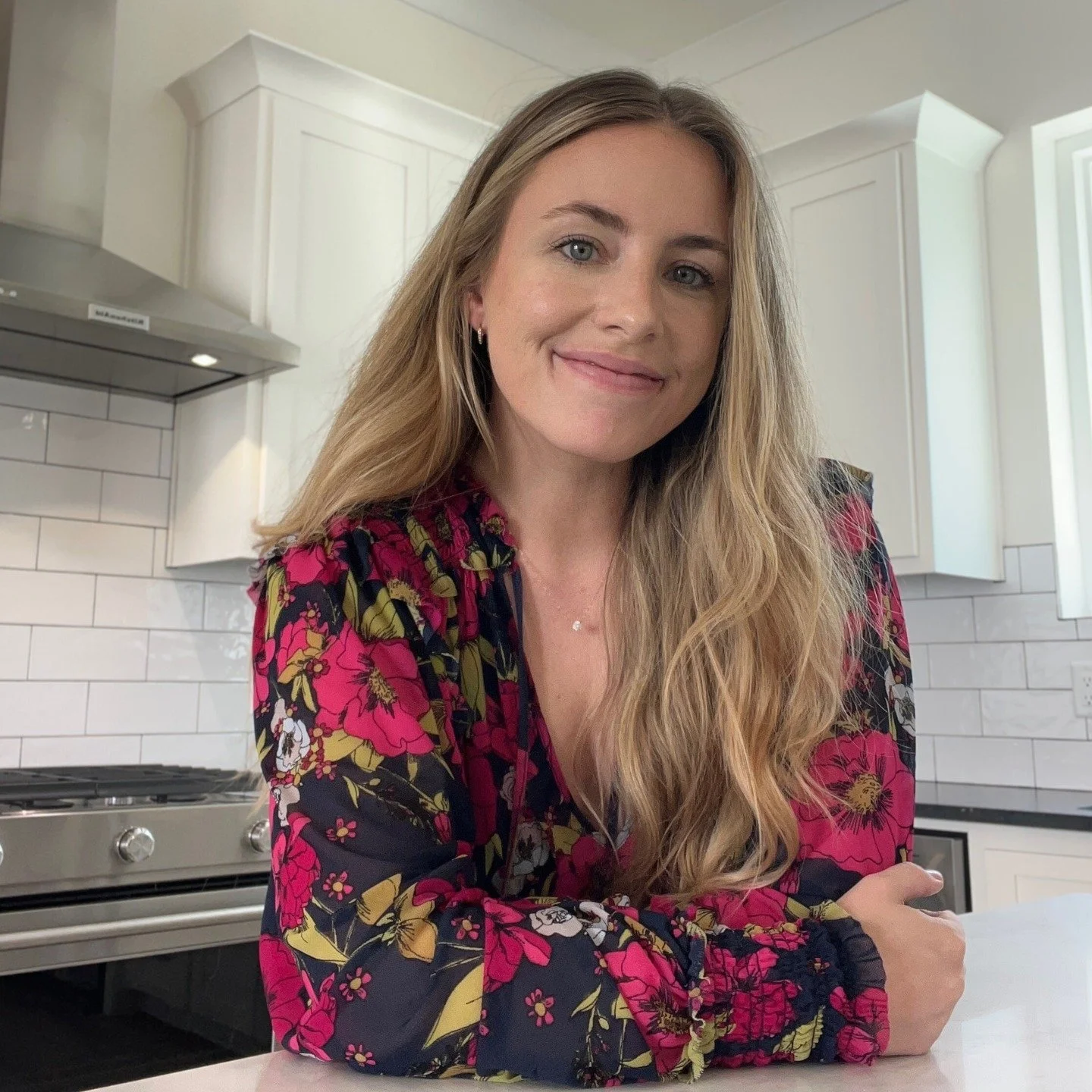 Nora Trotman smiling in a modern kitchen with white cabinets and a stainless steel stove.