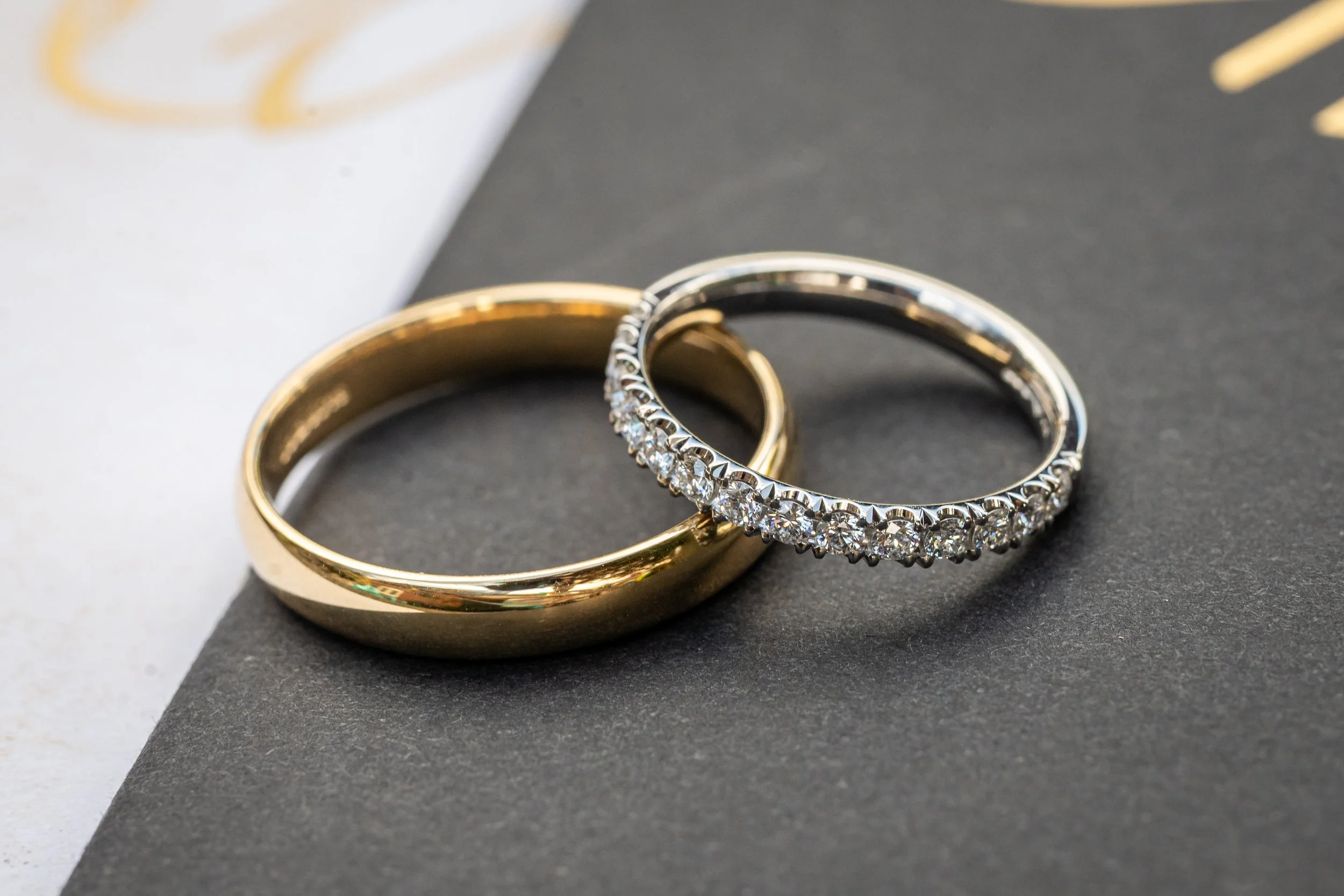 Two rings, one gold and one silver with diamonds, resting on a black surface with a white background.
