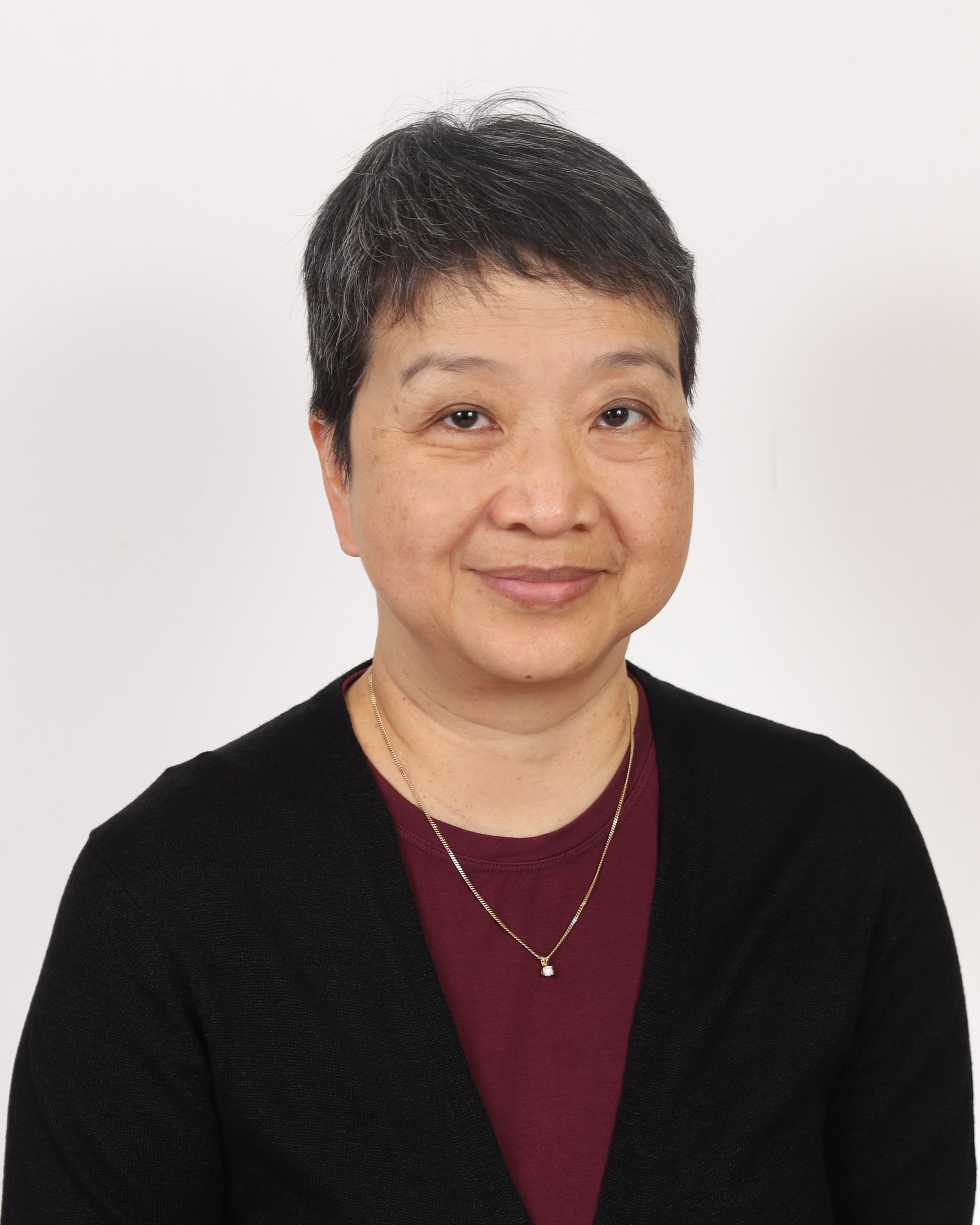A woman with short dark hair, glasses, and a red collared shirt posing against a black background.