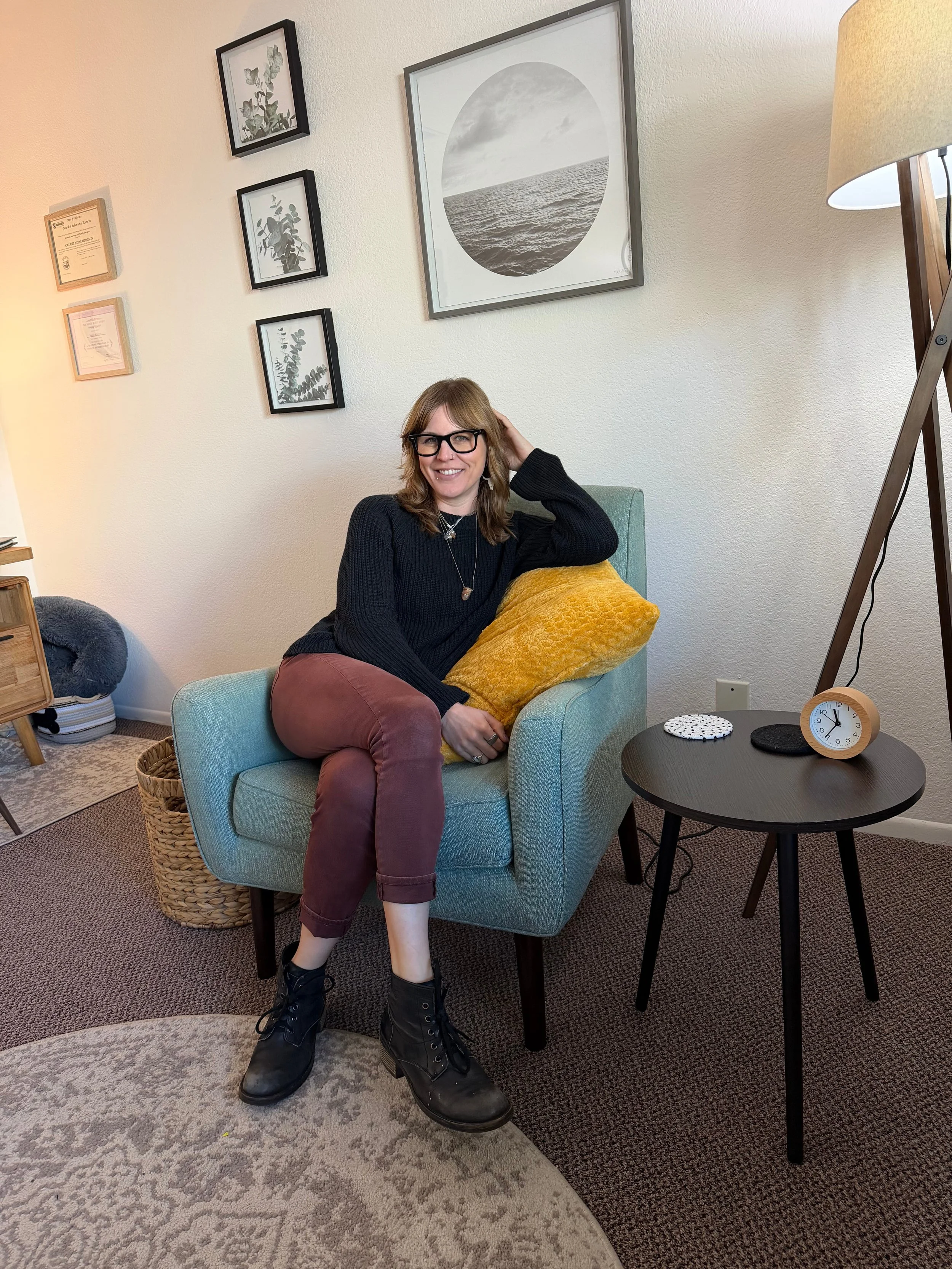 Natalie sitting in a chair, relaxed and smiling, in a well-lit room with neutral decor.