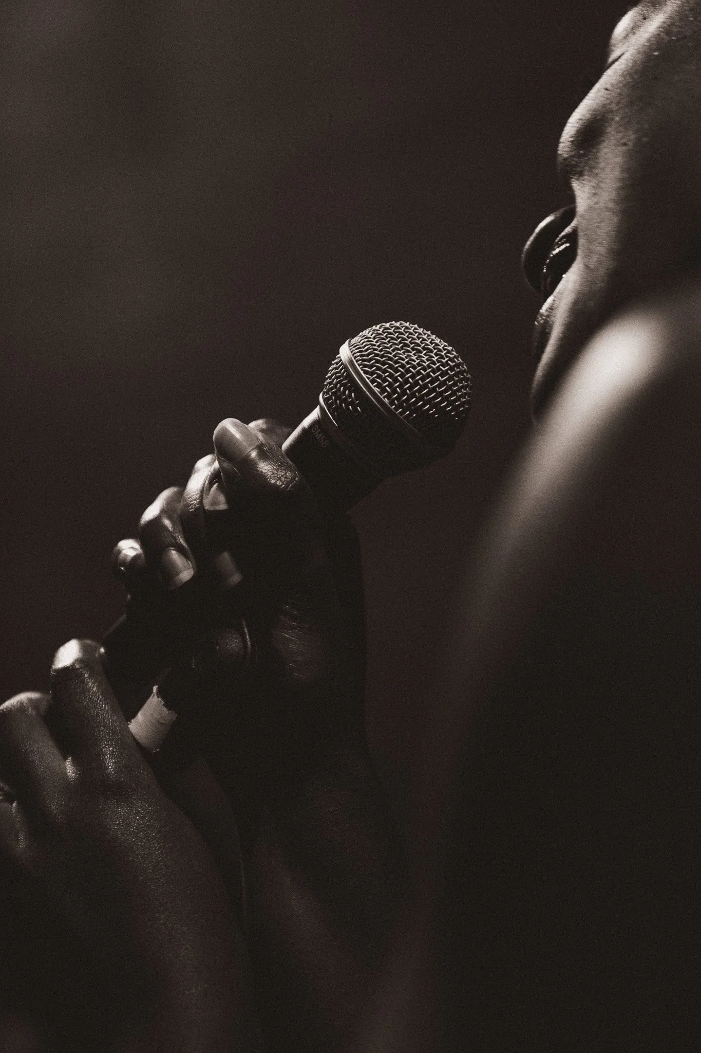 Close-up of a person holding a microphone with their face partially visible in the background, in black and white.