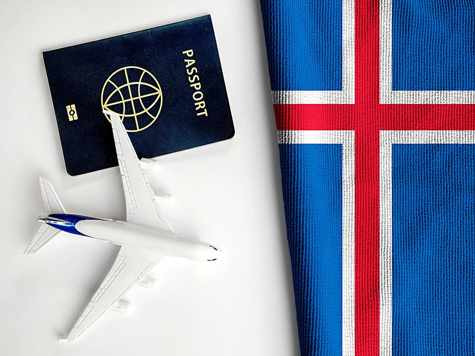 A passport and a model airplane beside the flag of Iceland