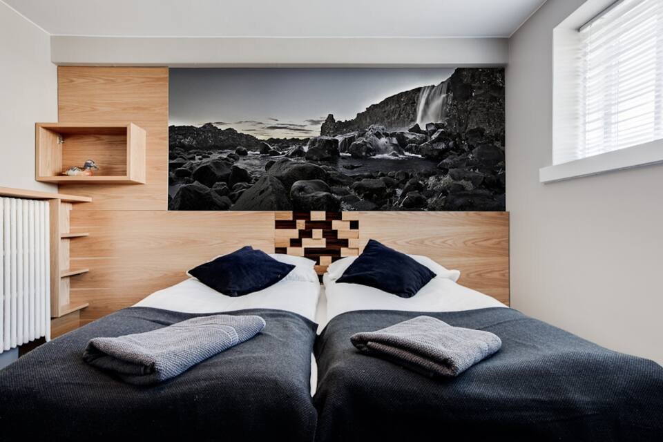Bedroom with a black and white panorama of Öxarárfoss waterfall above a pale oak headboard, twin beds pushed together