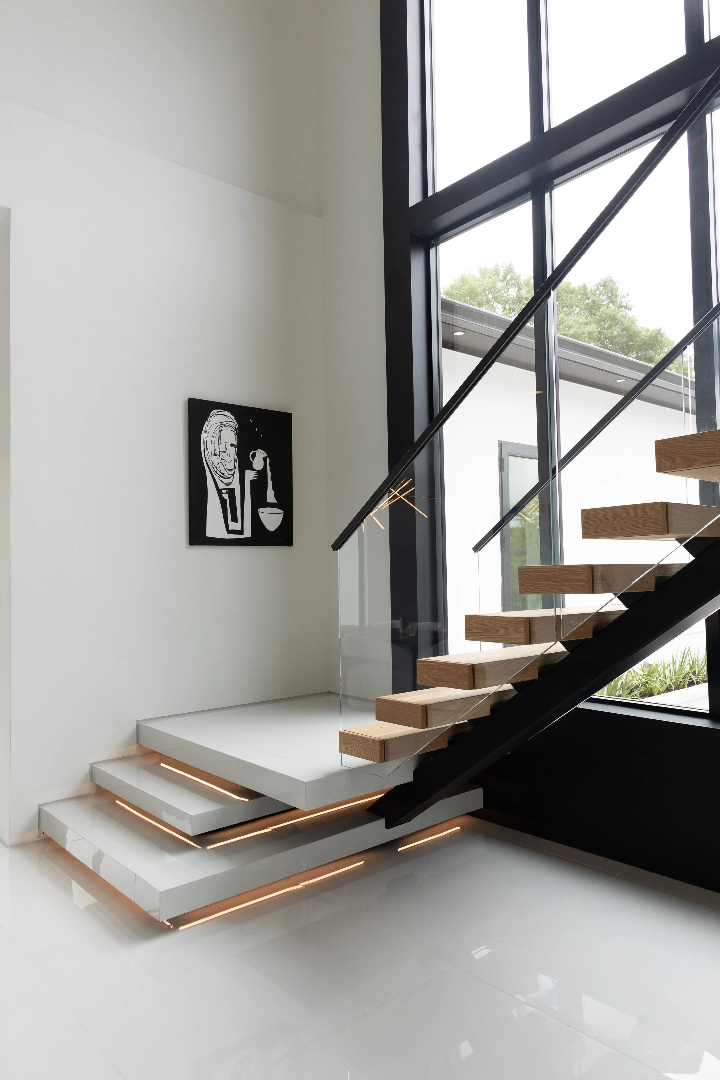 Modern floating staircase with warm wood treads, glass railing, and LED step lighting in a custom luxury home in Baton Rouge, LA