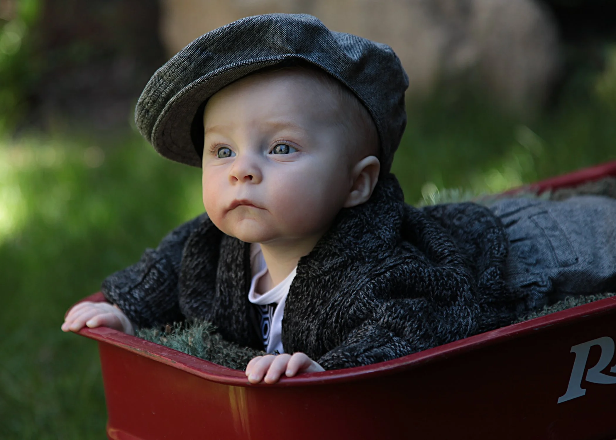 baby boy wearing newsboy cap peeking from red wagon.JPG