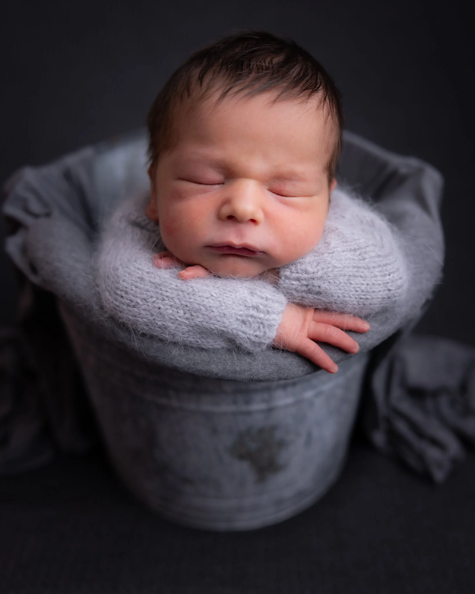 Close-up of a sleeping baby with a fuzzy blanket, lying on a dark surface.