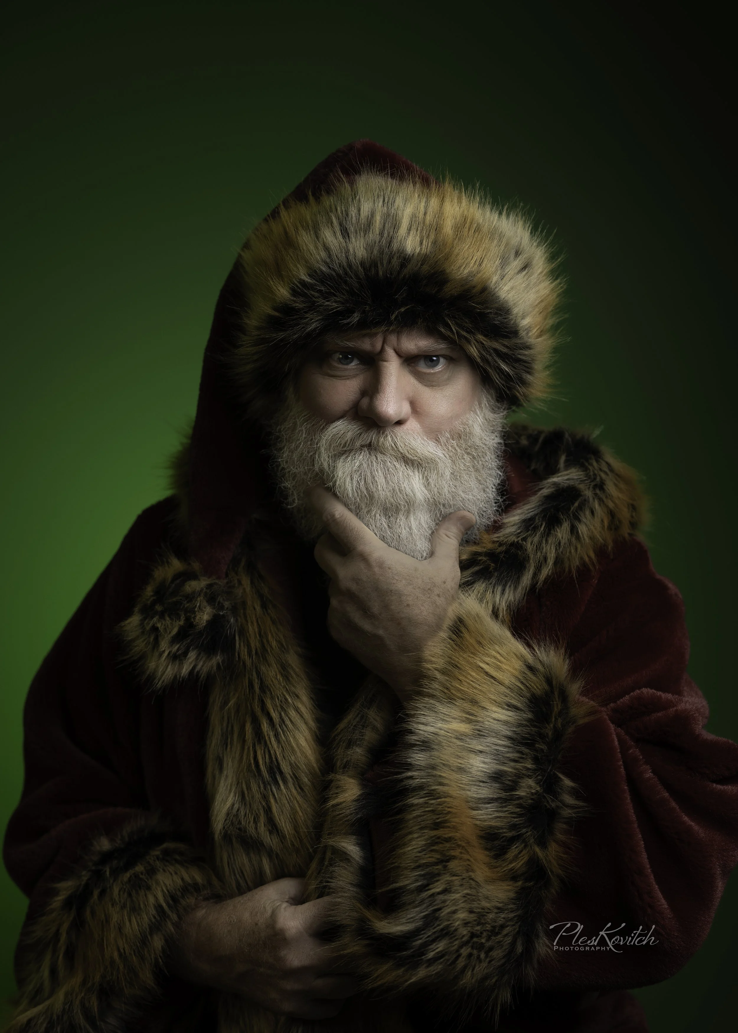 A man with a white beard and blue eyes wears a fur hat and coat, holding a large tiger with orange and black striped fur against a green background.