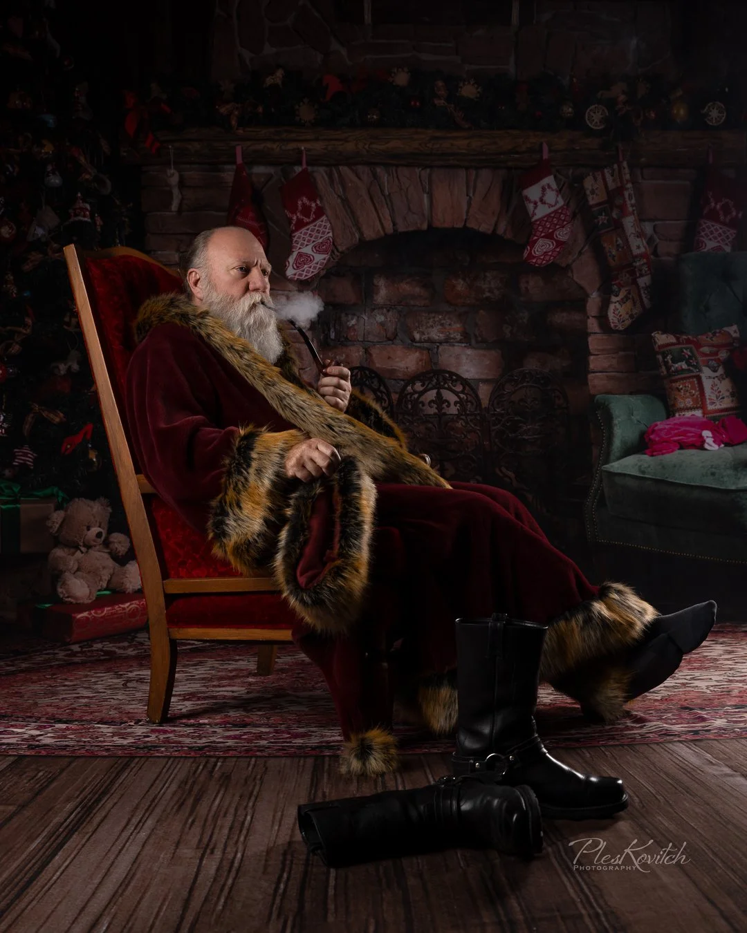 Santa Claus sitting in a red velvet chair, smoking a pipe in a cozy, Christmas decorated living room with stockings hanging by a brick fireplace, Christmas tree, and wrapped presents.