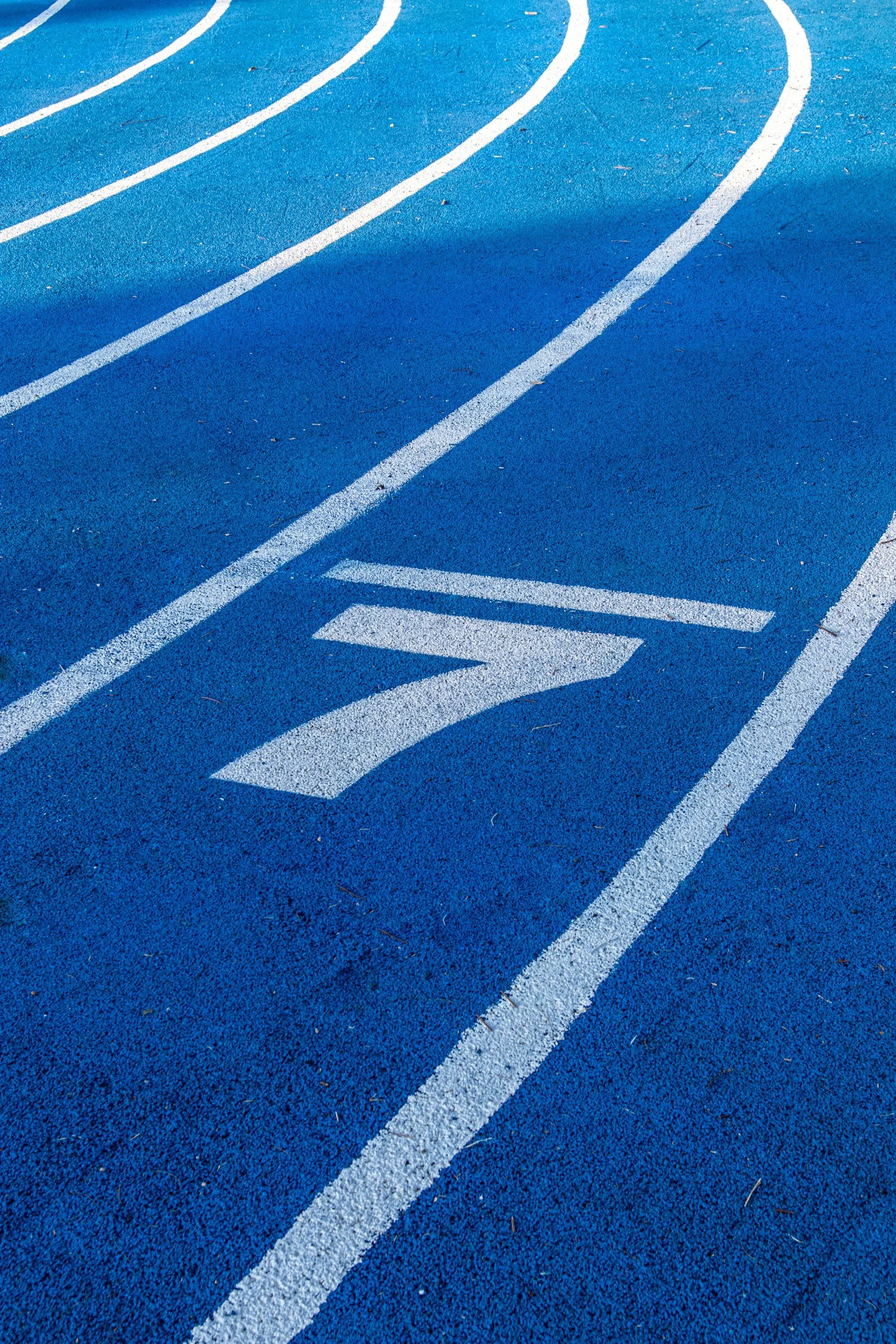 A close-up of a blue running track with white lane markings.